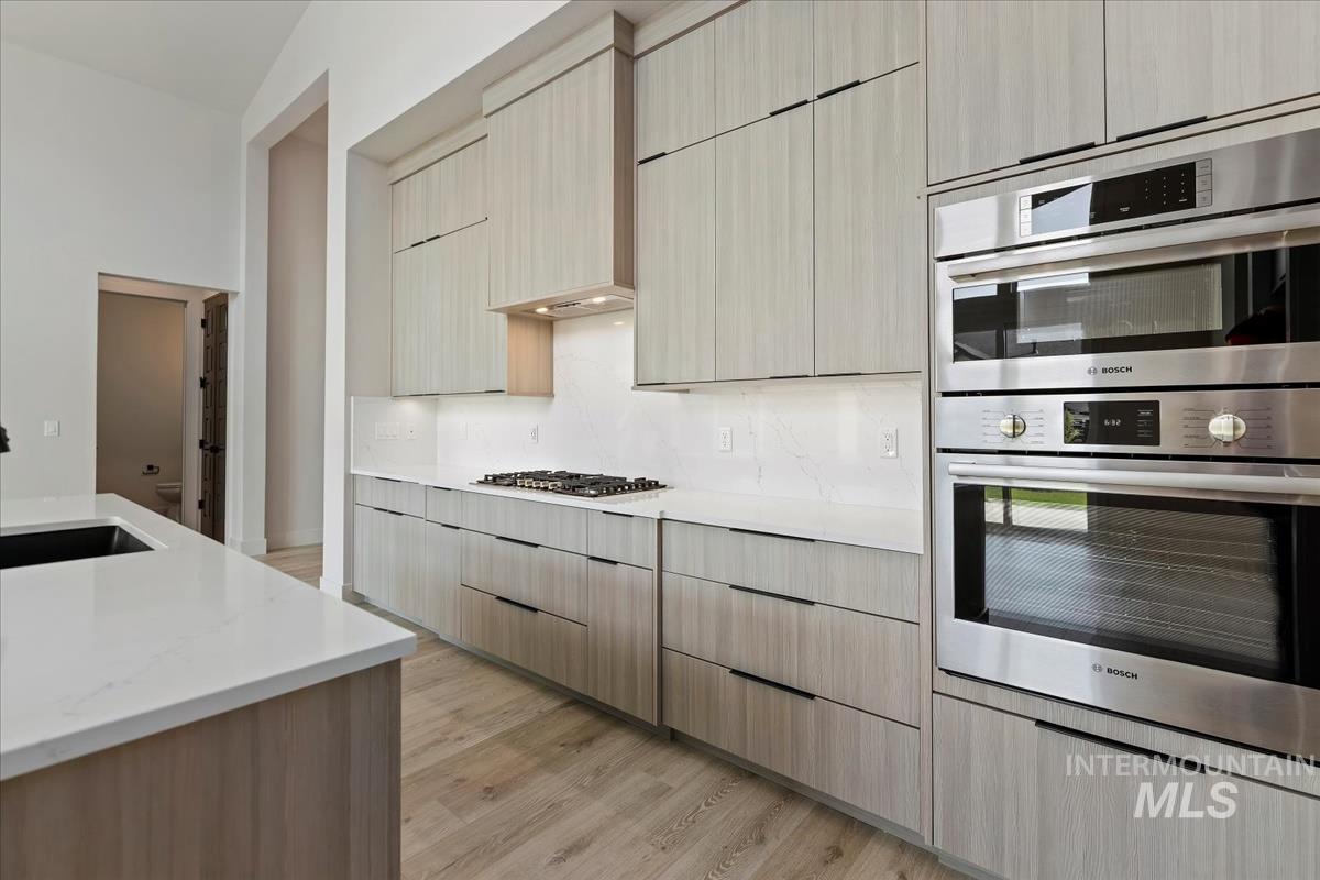 Kitchen with appliances with stainless steel finishes, light stone counters, light wood finished floors, light brown cabinets, and modern cabinets