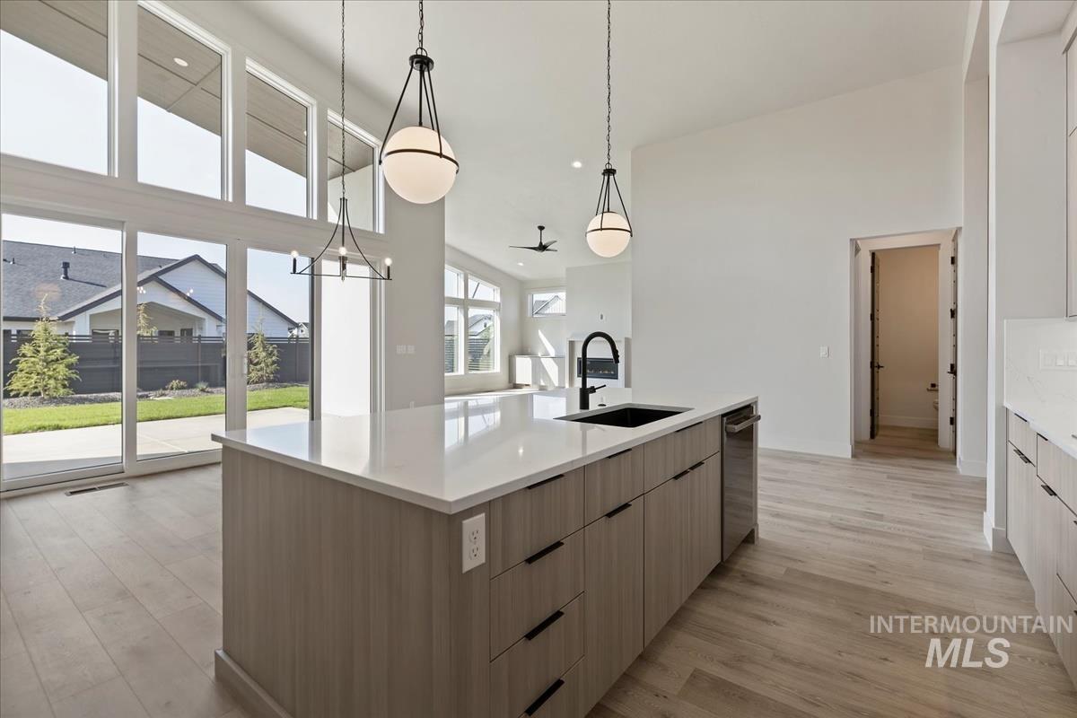 Kitchen featuring a large island with sink, light wood finished floors, hanging light fixtures, open floor plan, and light stone counters