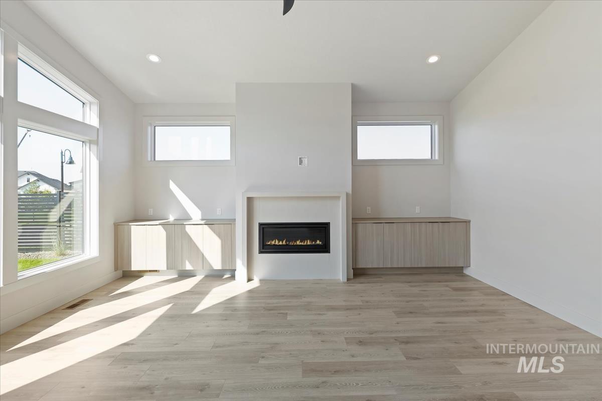Unfurnished living room with light wood-style floors, a glass covered fireplace, and recessed lighting