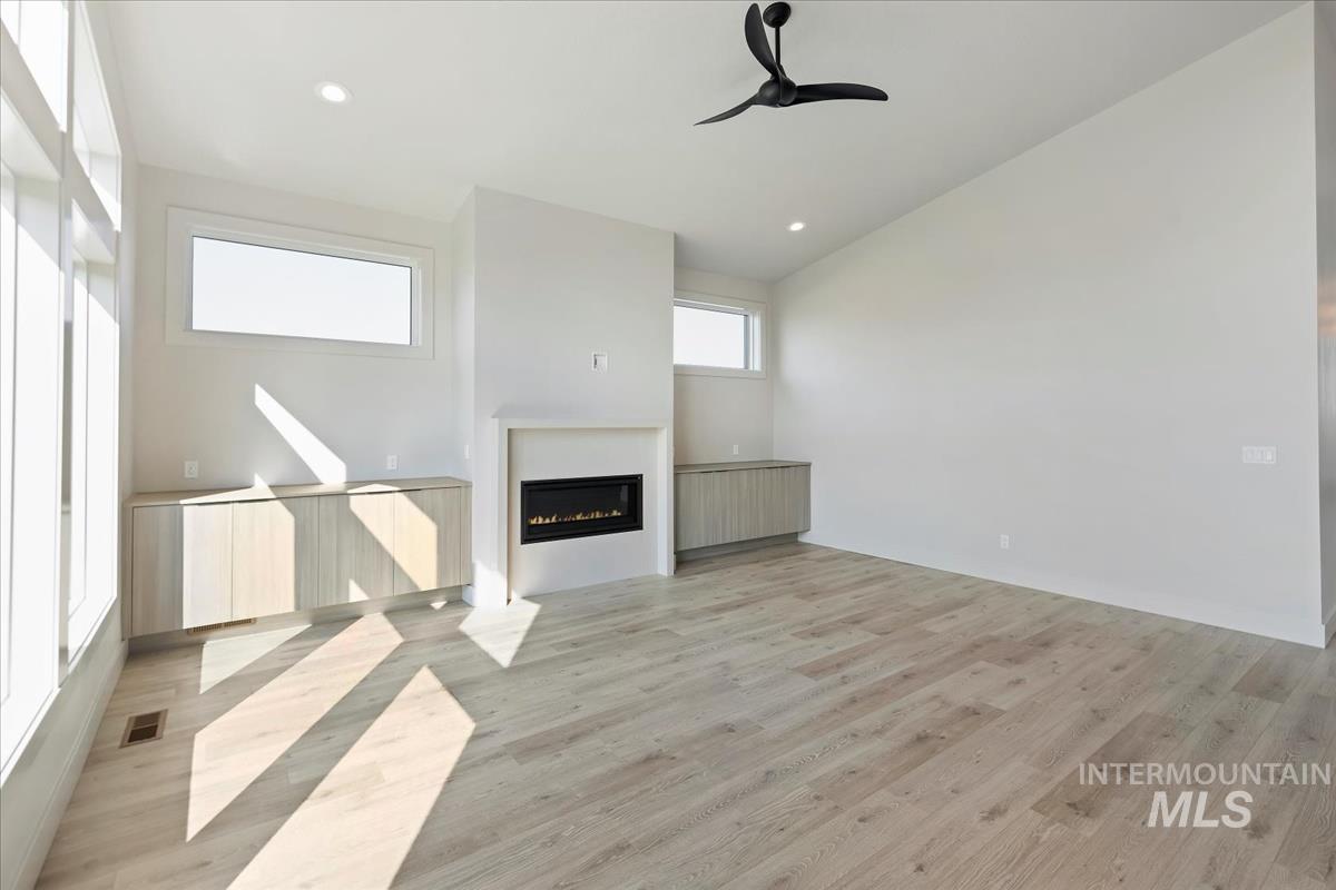 Unfurnished living room featuring light wood-style flooring, recessed lighting, a glass covered fireplace, and a ceiling fan