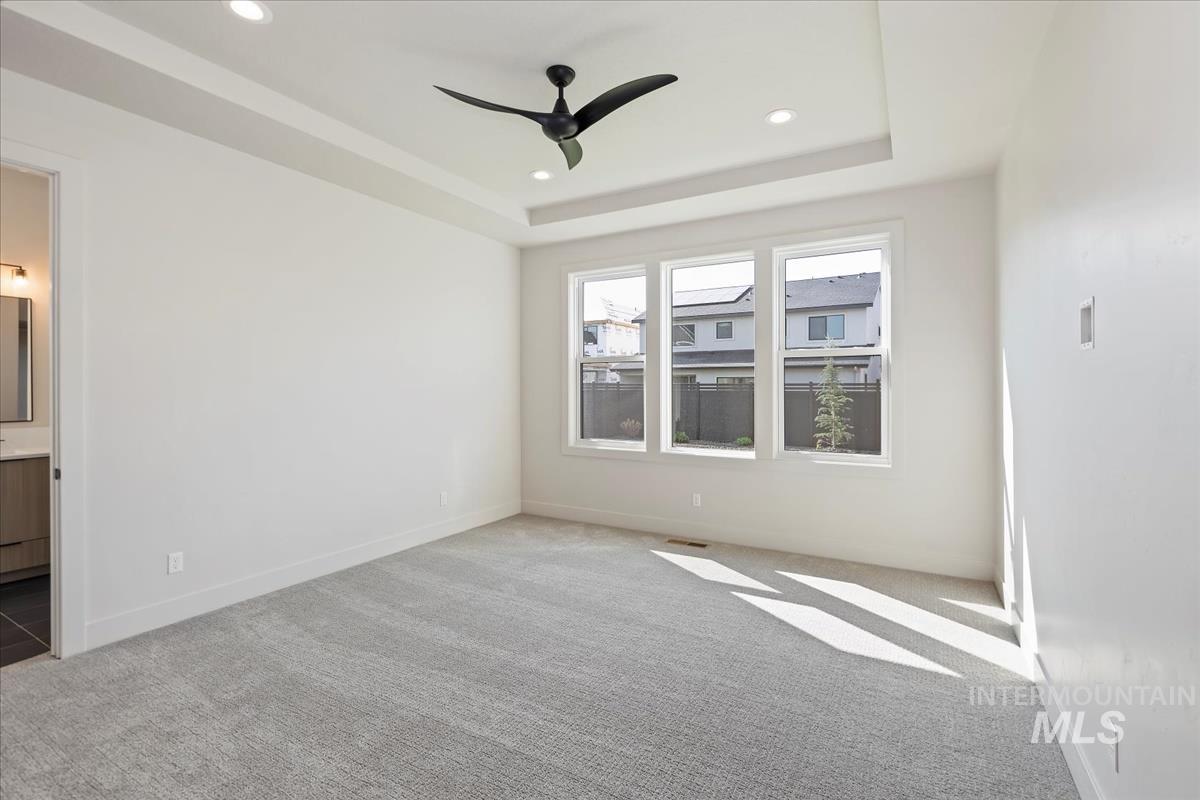 Unfurnished bedroom featuring carpet, a raised ceiling, recessed lighting, ceiling fan, and ensuite bathroom
