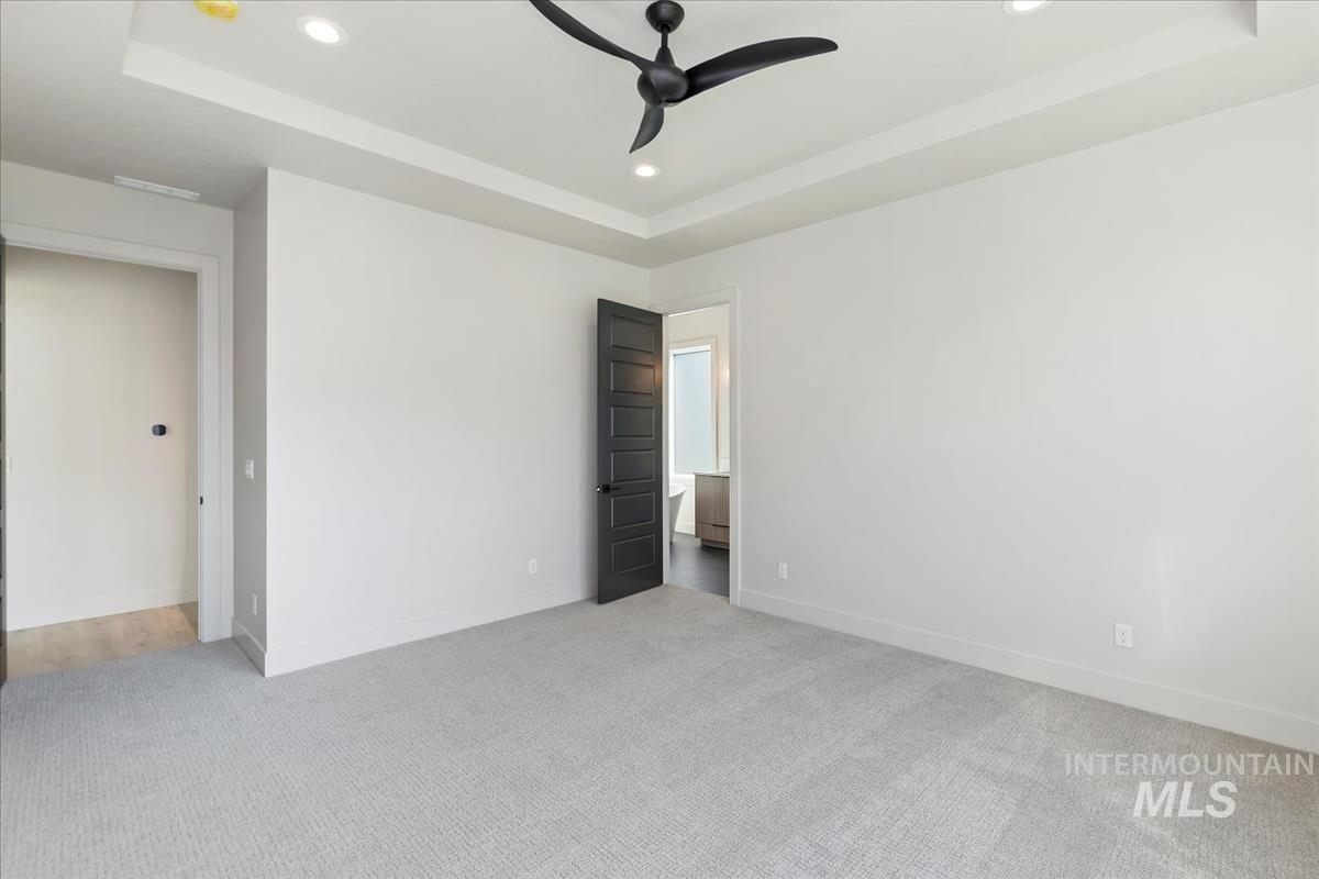 Unfurnished bedroom featuring a raised ceiling, light carpet, recessed lighting, and a ceiling fan