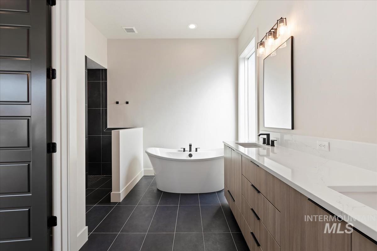 Bathroom with a freestanding tub, dark tile patterned flooring, double vanity, a walk in shower, and recessed lighting