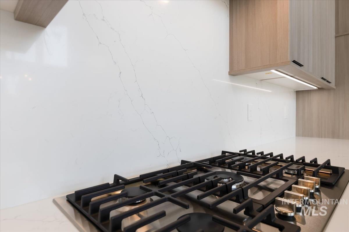 Kitchen view of stainless steel gas stovetop, light brown cabinets, light stone counters, and modern cabinets