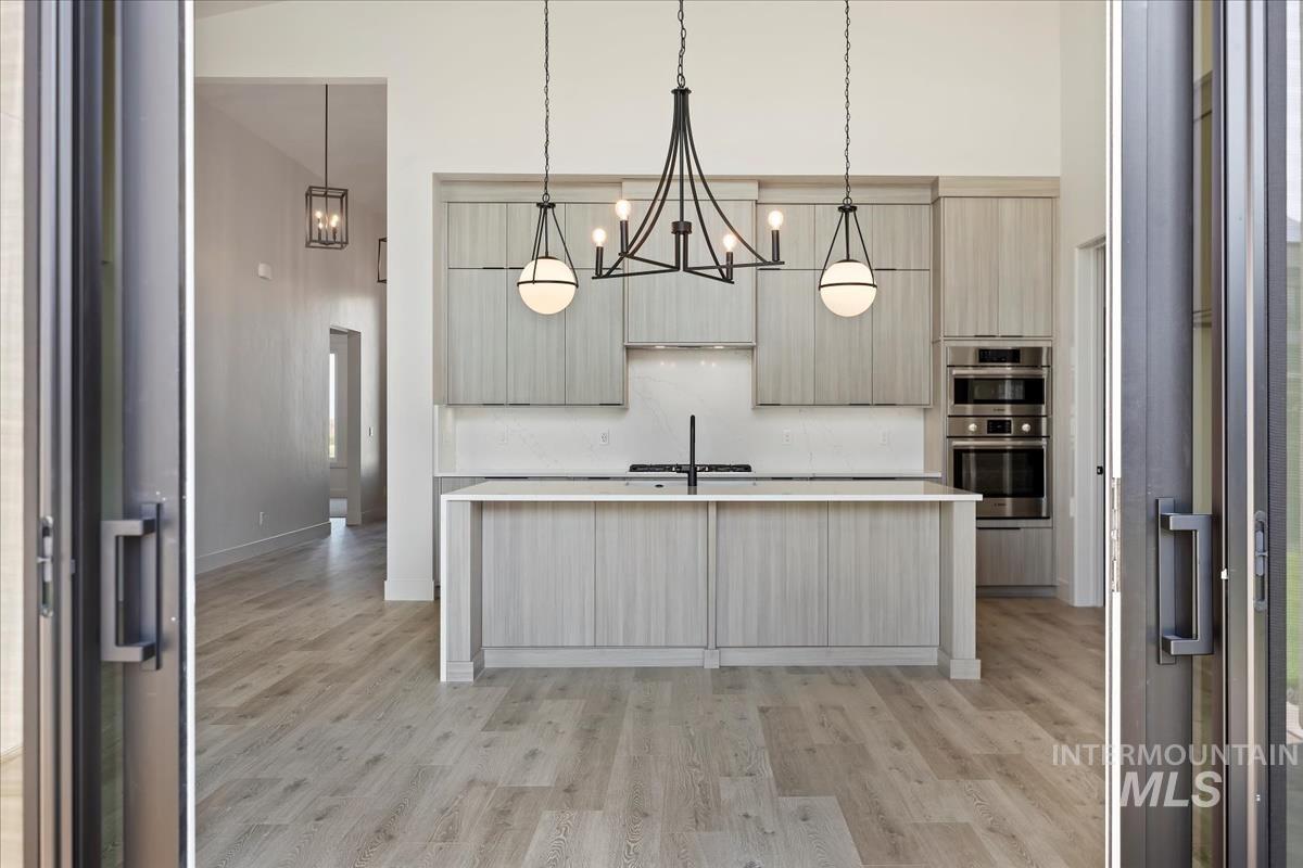 Kitchen featuring modern cabinets, an island with sink, light wood-style flooring, pendant lighting, and a towering ceiling