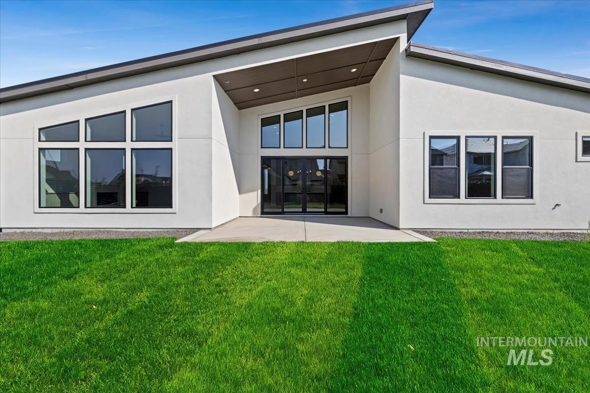 Rear view of property featuring a patio, a lawn, and stucco siding