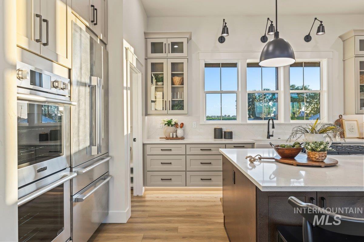 Kitchen featuring glass insert cabinets, light stone counters, pendant lighting, backsplash, and stainless steel appliances