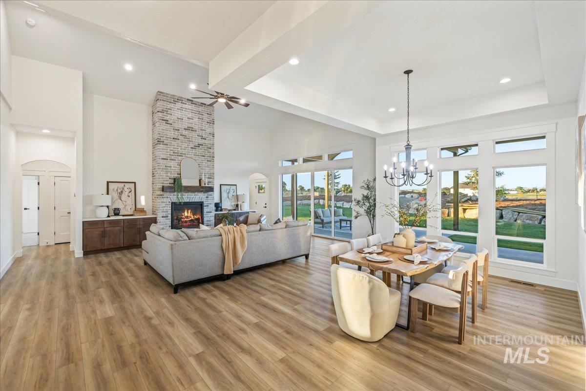 Dining space featuring a raised ceiling, a brick fireplace, ceiling fan, light wood finished floors, and recessed lighting