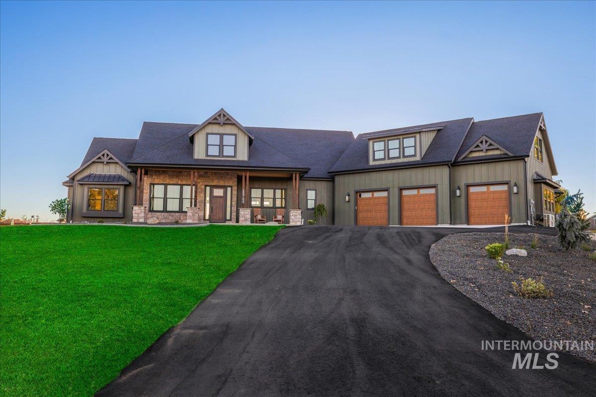 Craftsman house featuring driveway, covered porch, stone siding, a front yard, and board and batten siding