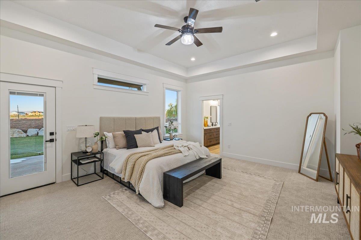 Bedroom with light colored carpet, a tray ceiling, ensuite bathroom, and recessed lighting