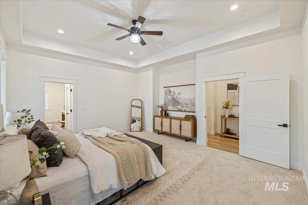Carpeted bedroom featuring a raised ceiling, recessed lighting, and a ceiling fan
