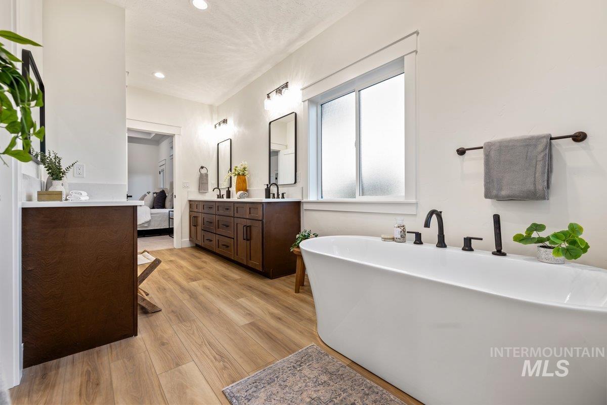 Ensuite bathroom featuring double vanity, a soaking tub, light wood finished floors, recessed lighting, and a textured ceiling