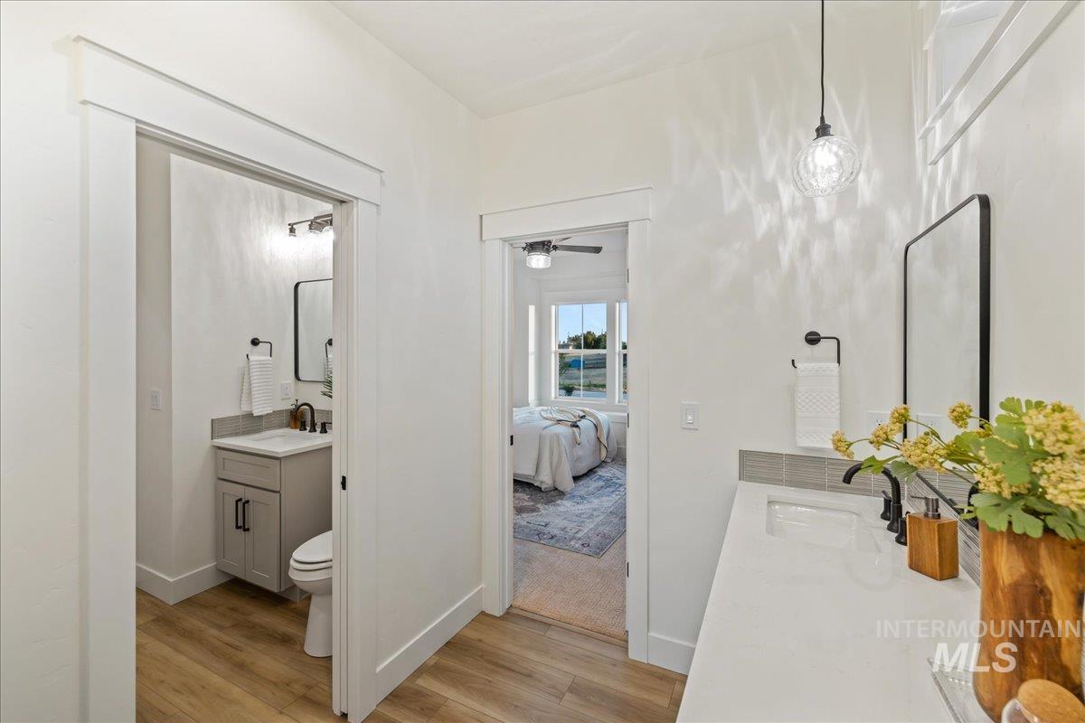 Ensuite bathroom with two vanities, light wood-style floors, and a ceiling fan