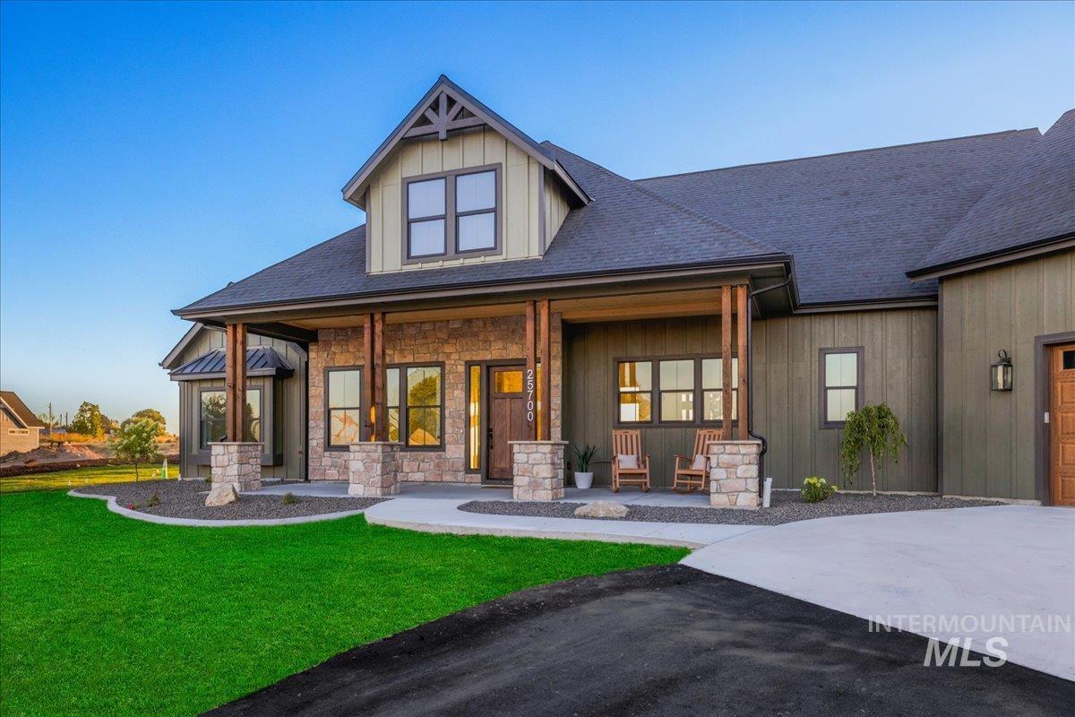 View of front of house featuring a porch, a shingled roof, a front yard, and stone siding
