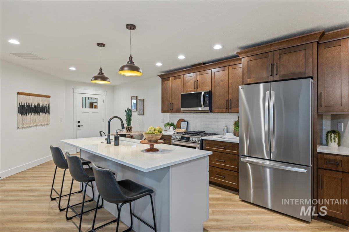 Kitchen with stainless steel appliances, hanging light fixtures, a breakfast bar, decorative backsplash, and light wood-style flooring