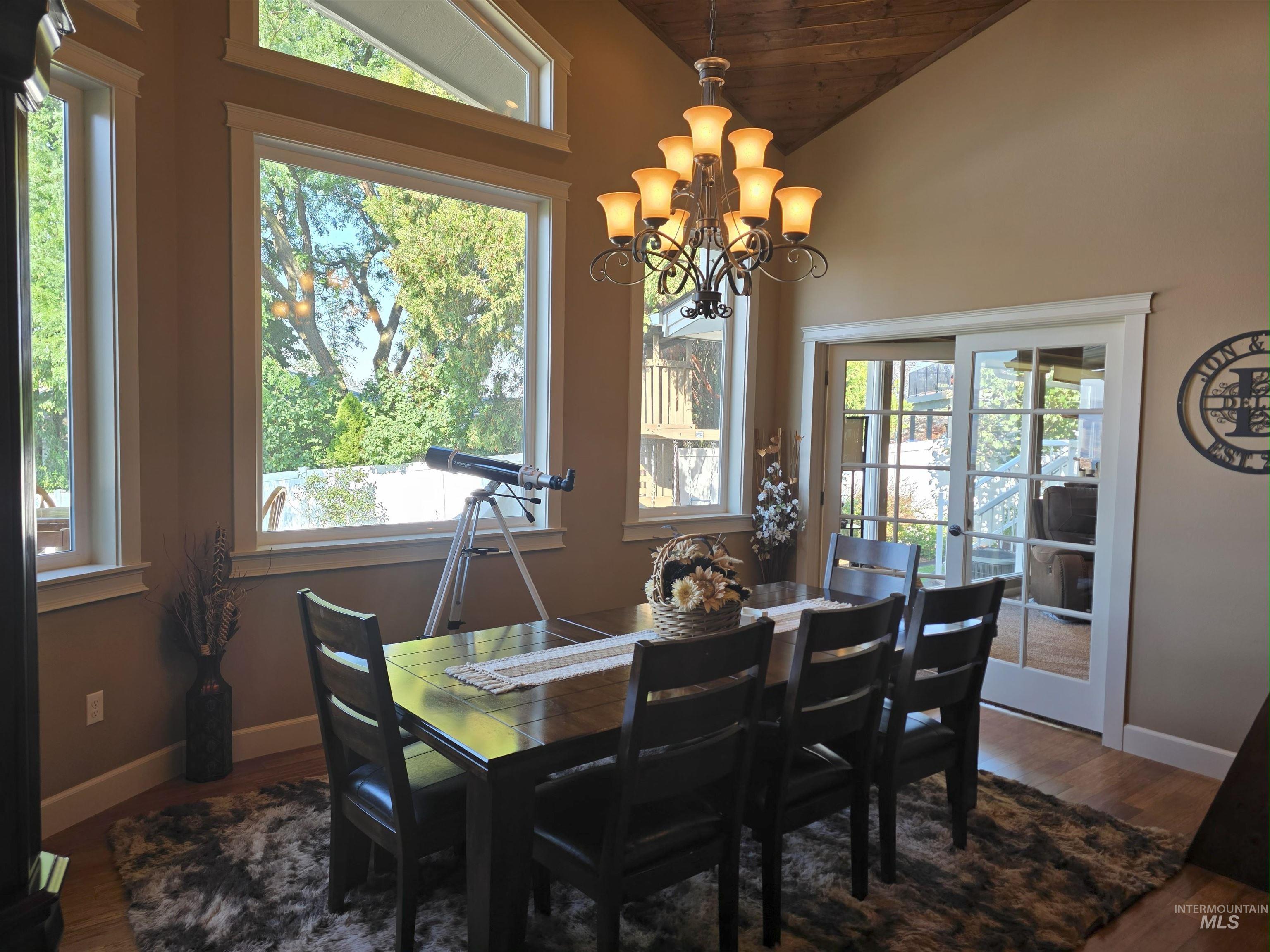 Dining area with dark wood-type flooring, vaulted ceiling, a chandelier, french doors, and wooden ceiling