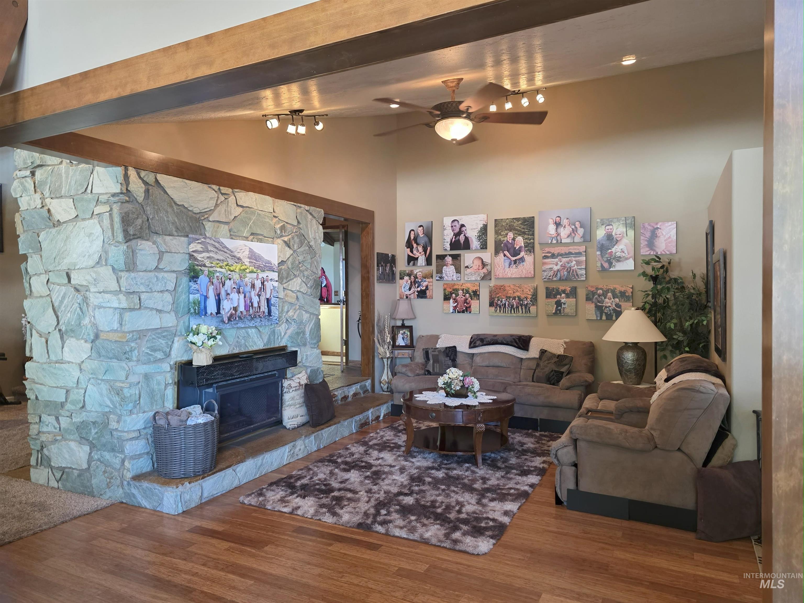 Living area with a ceiling fan, wood finished floors, a fireplace, beamed ceiling, and high vaulted ceiling