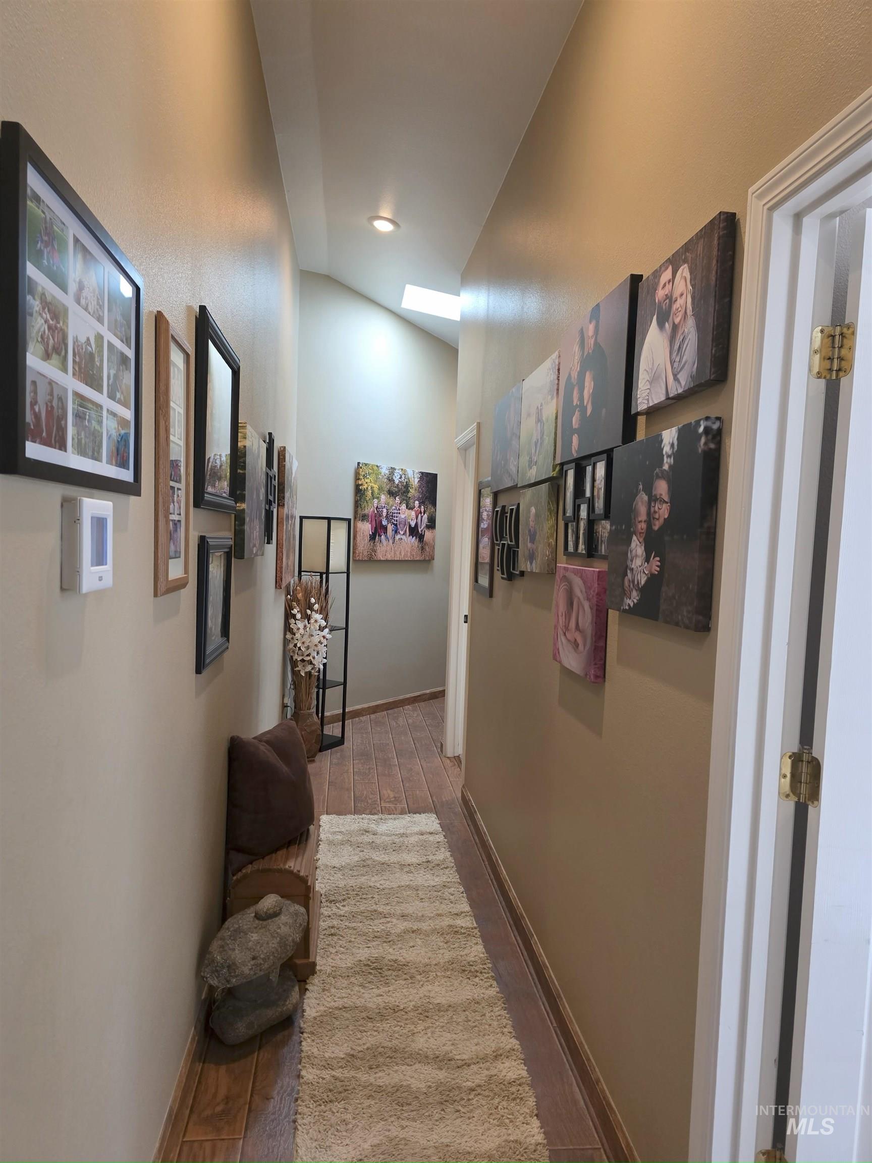 Corridor with wood finished floors and lofted ceiling