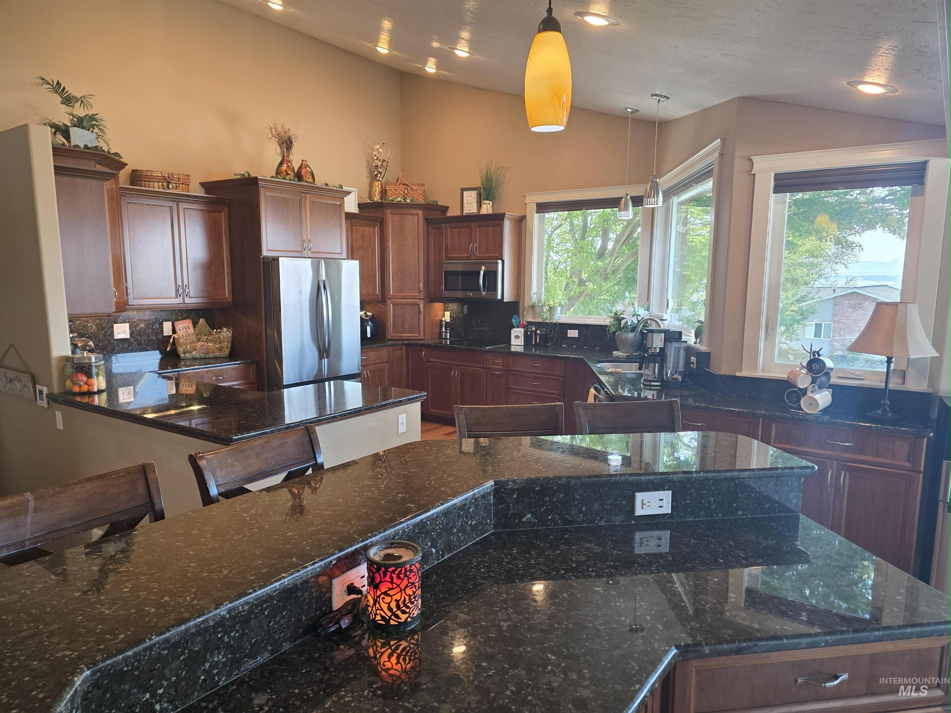 Kitchen featuring dark stone counters, vaulted ceiling, stainless steel appliances, decorative light fixtures, and backsplash