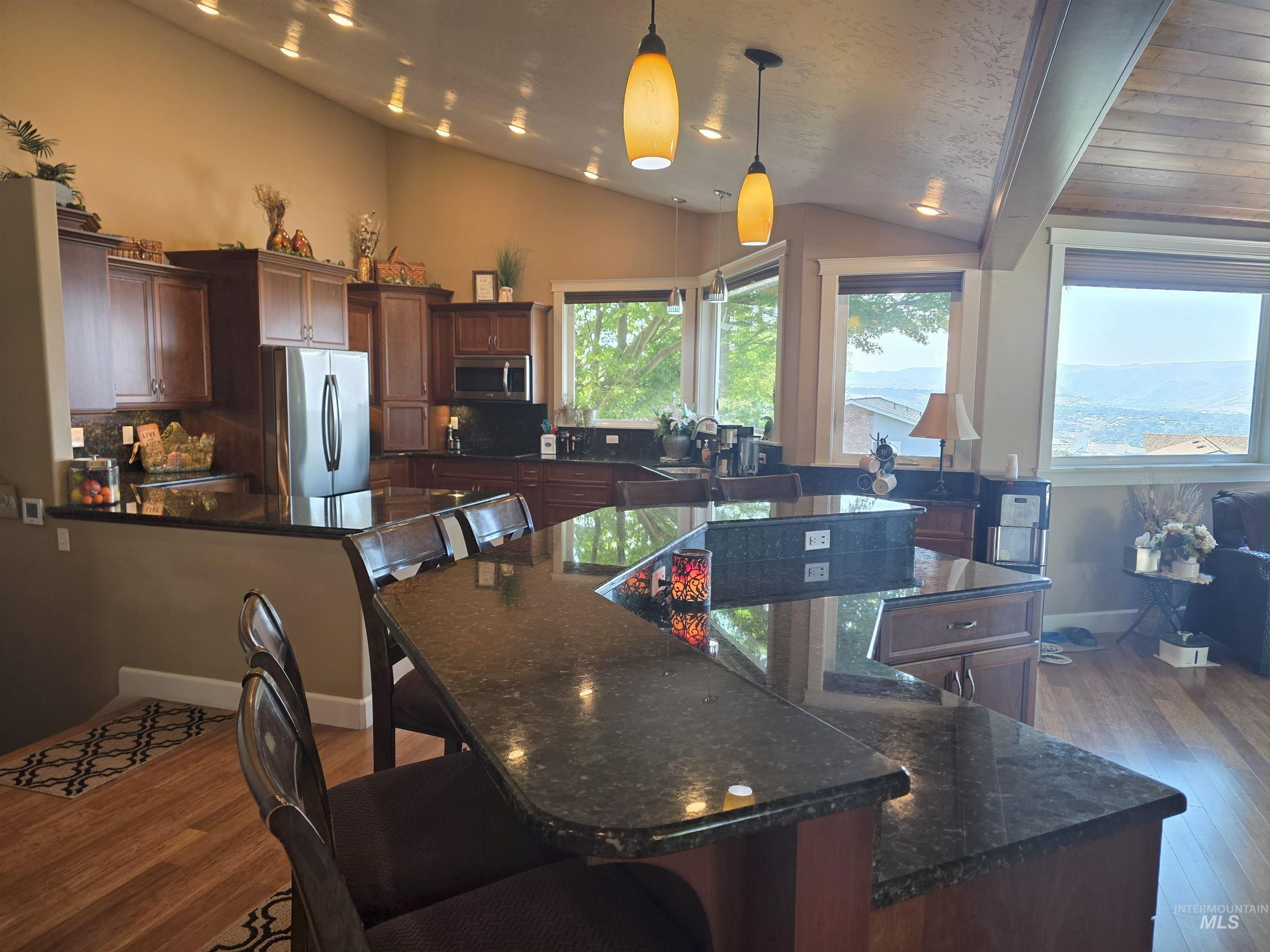 Kitchen featuring lofted ceiling, decorative backsplash, dark stone countertops, stainless steel appliances, and hanging light fixtures