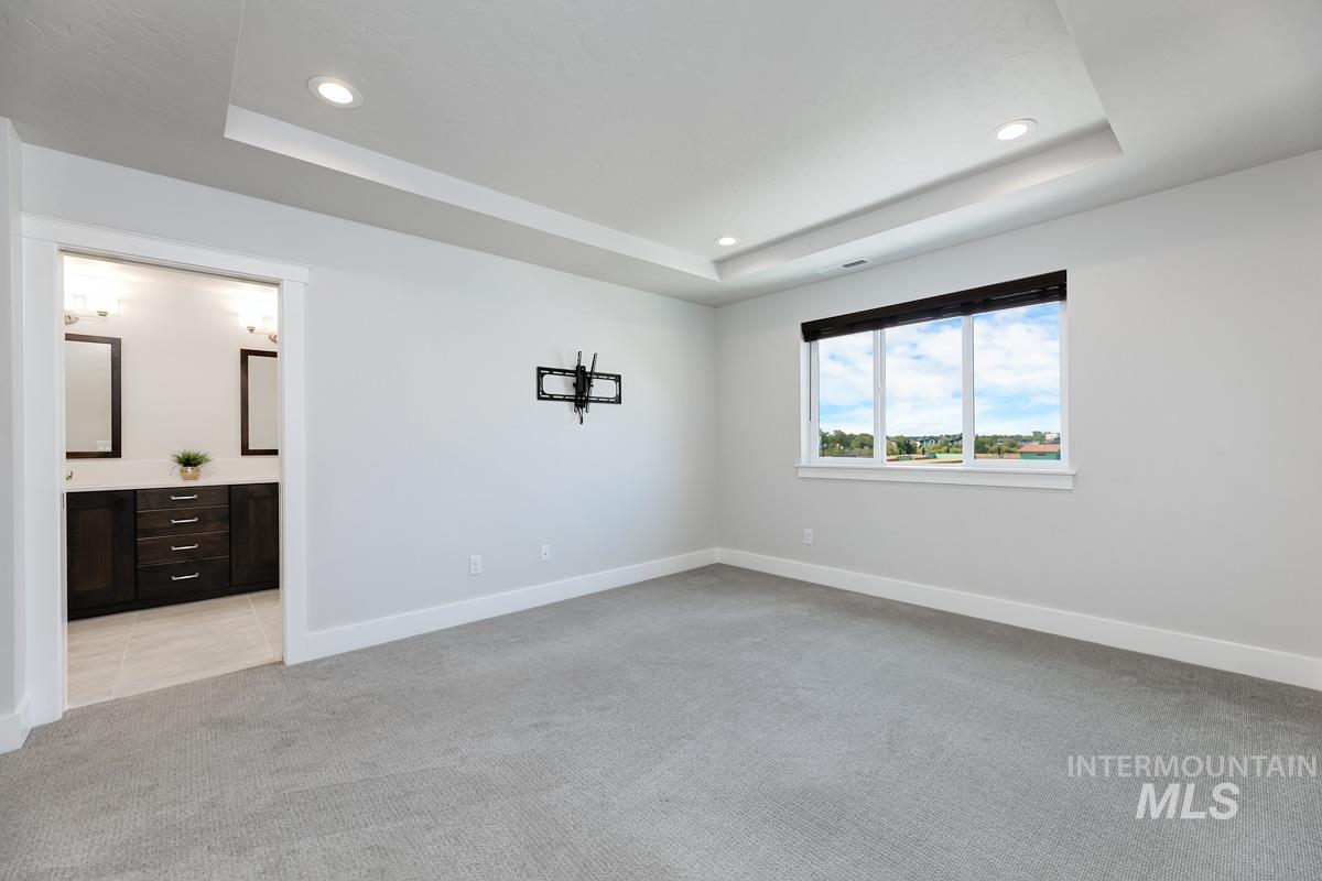 Large primary bedroom with a tray ceiling, light carpet, recessed lighting, and ensuite bath