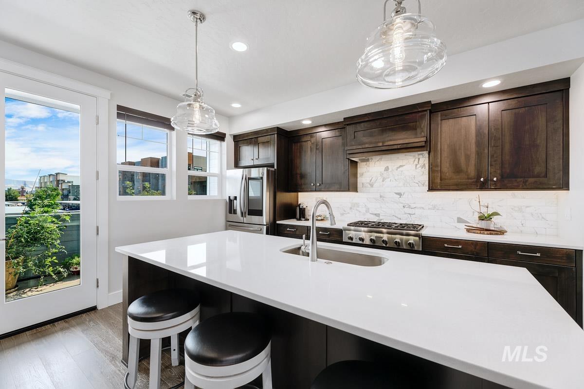 Kitchen with dark brown cabinetry, tasteful backsplash, decorative light fixtures, light wood-style flooring, and stainless steel appliances