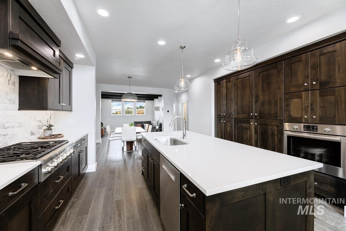 Kitchen with an island with sink, dark wood-type flooring, stainless steel appliances, dark brown cabinets, and recessed lighting