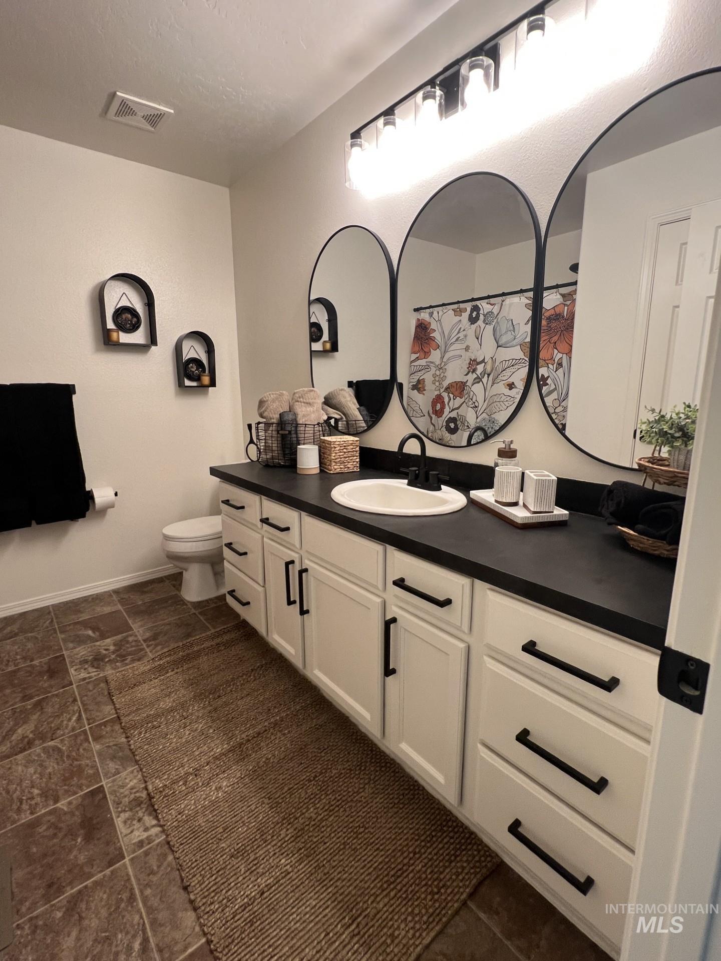Bathroom featuring vanity, curtained shower, and dark stone finish flooring