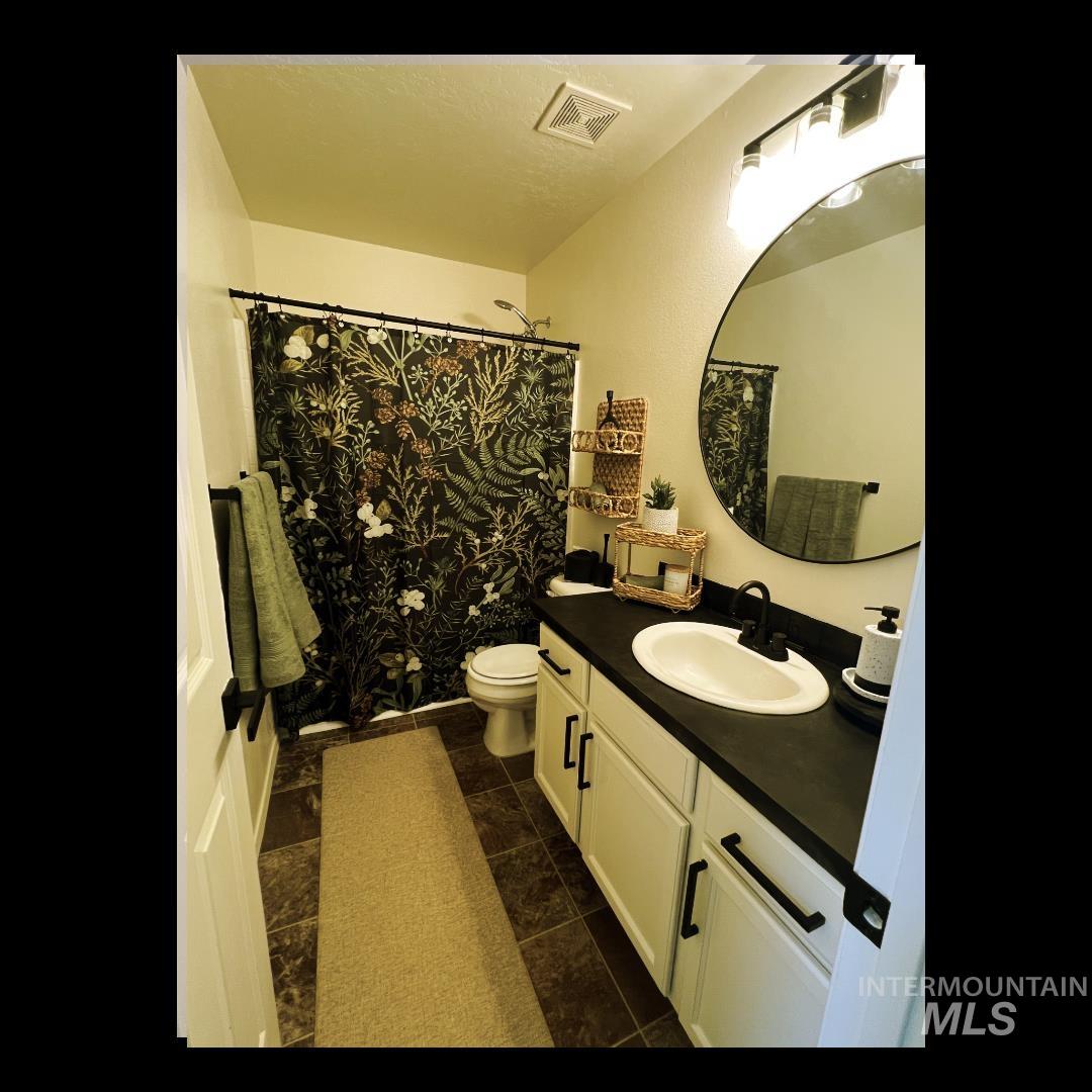 Full bath featuring vanity, dark tile patterned floors, a shower with shower curtain, and a textured ceiling