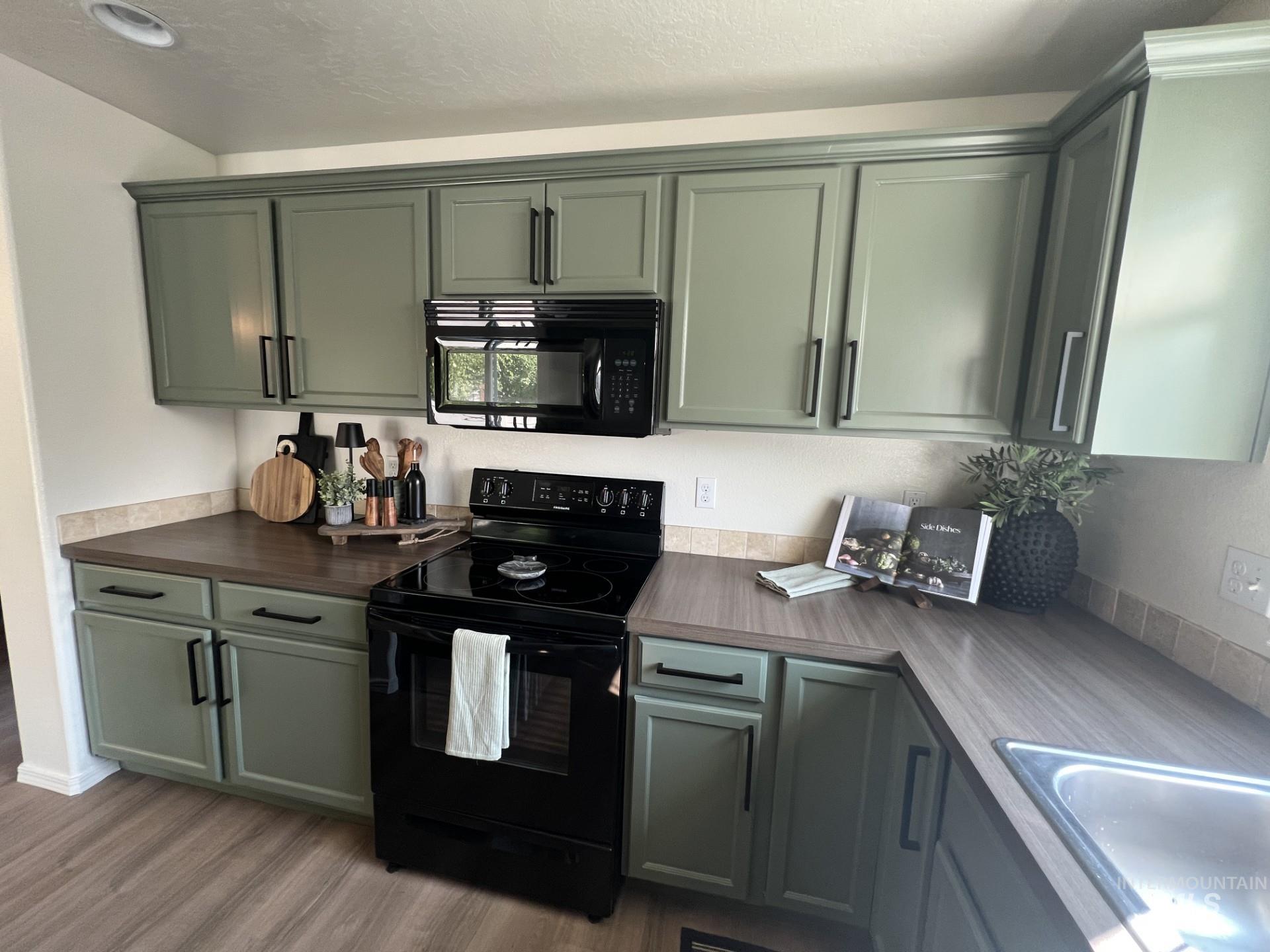 Kitchen featuring black appliances, light wood finished floors, green cabinets, a textured ceiling, and dark countertops