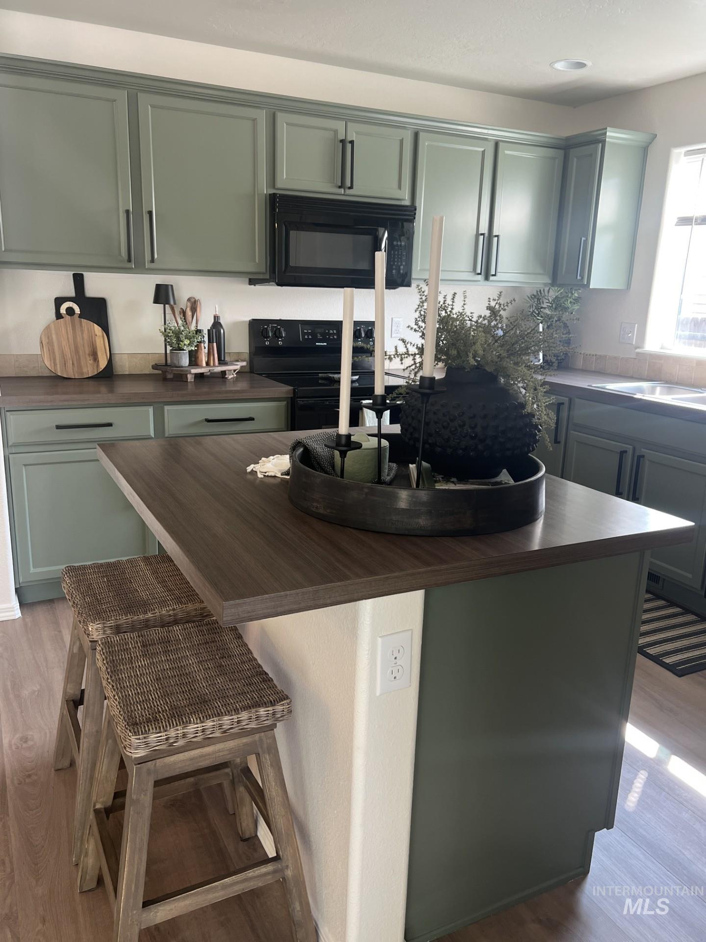 Kitchen featuring light wood-type flooring, green cabinets, and black appliances
