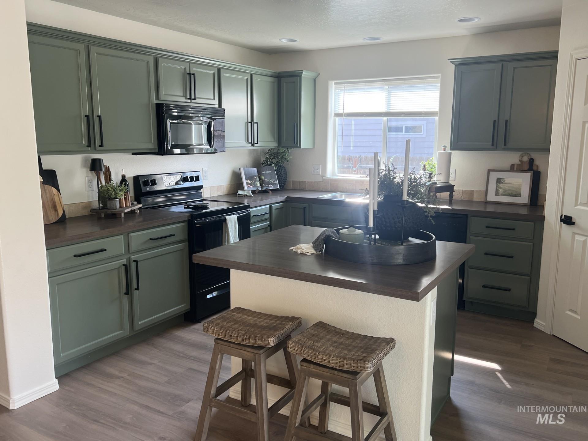 Kitchen with dark countertops, black appliances, a breakfast bar, dark wood-type flooring, and recessed lighting