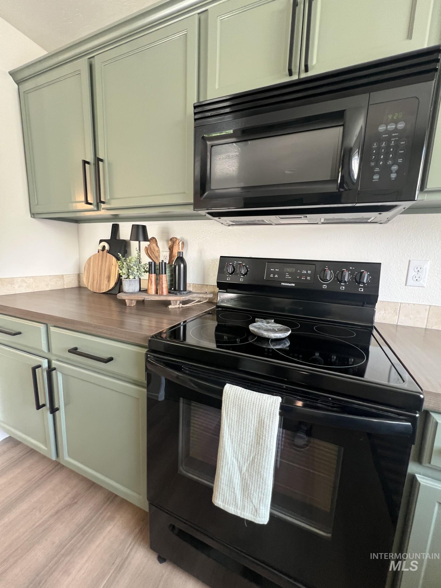 Kitchen featuring black appliances, green cabinetry, light wood-style floors, and dark countertops