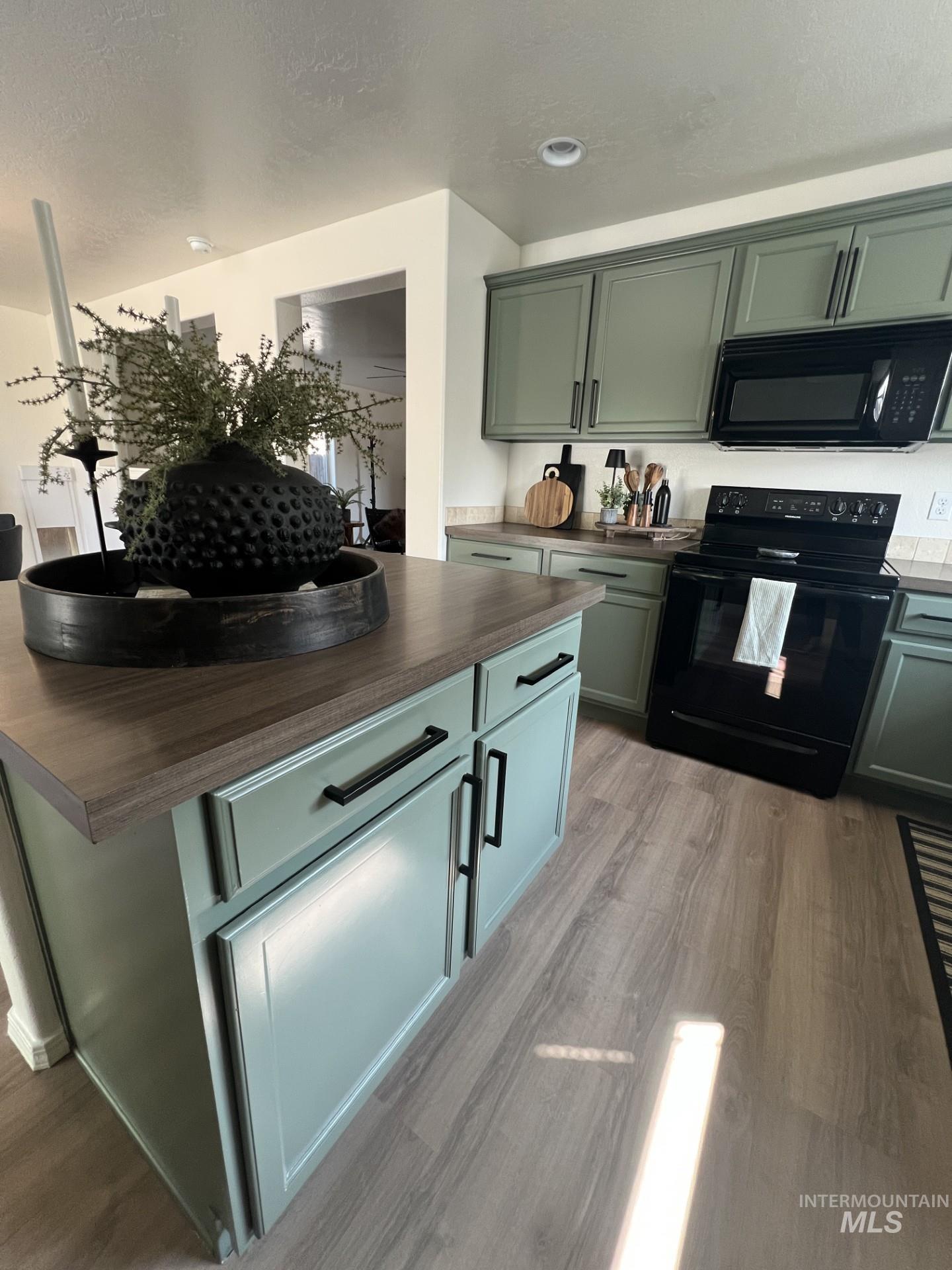 Kitchen with black appliances, green cabinetry, light wood-type flooring, and a textured ceiling