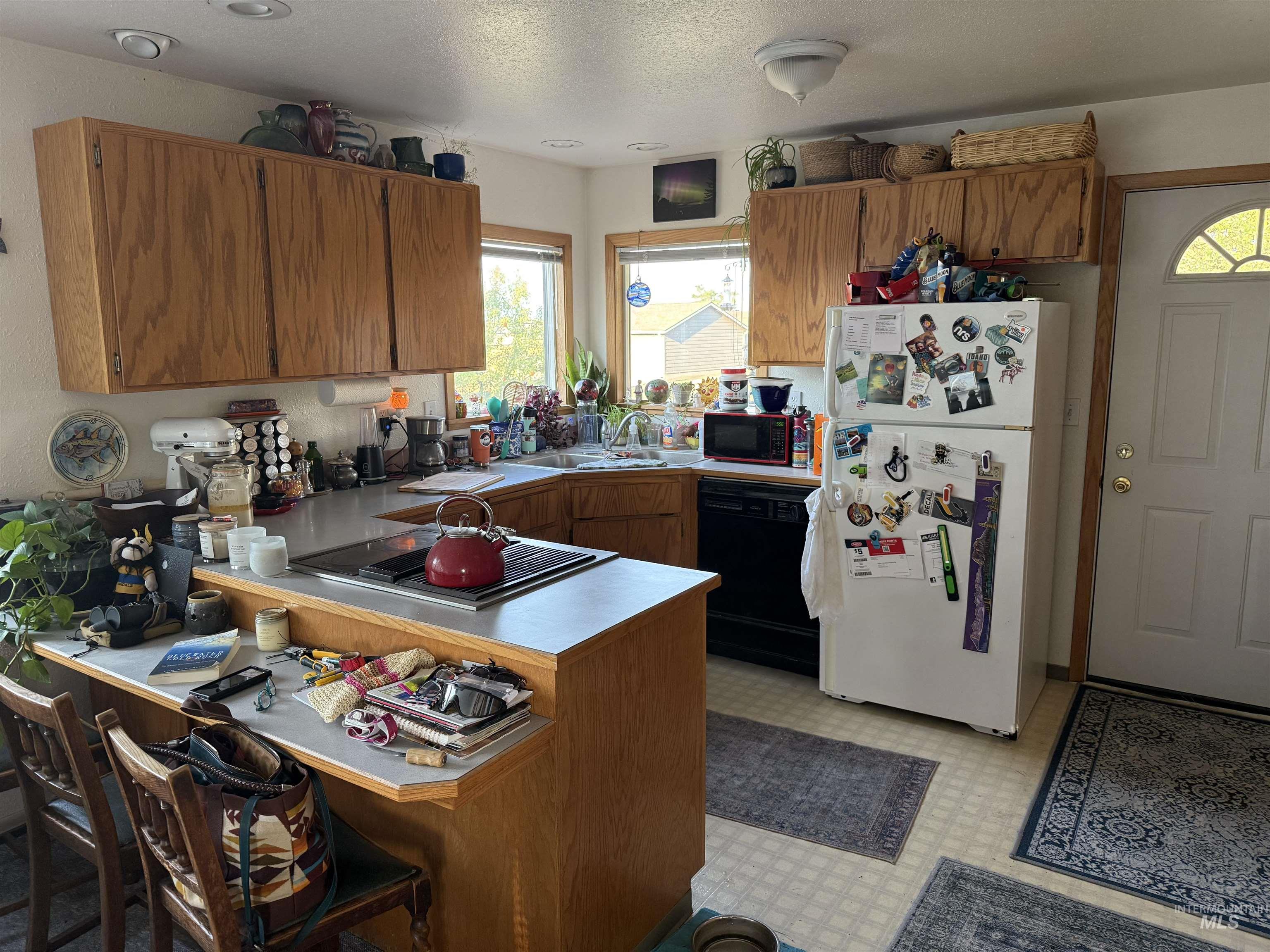 Kitchen featuring brown cabinetry, freestanding refrigerator, a peninsula, light countertops, and dishwasher