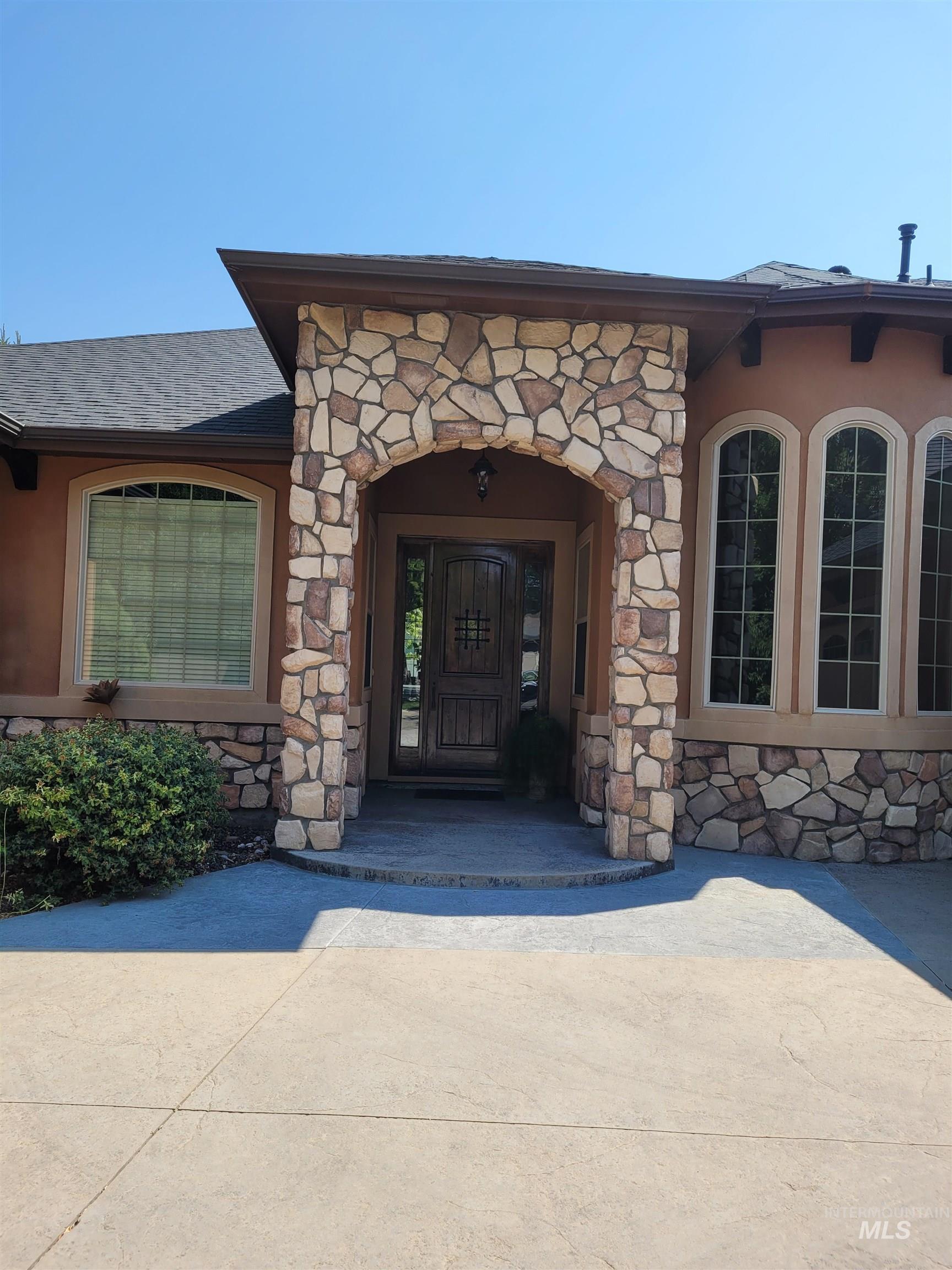 Doorway to property featuring stone siding, roof with shingles, and stucco siding