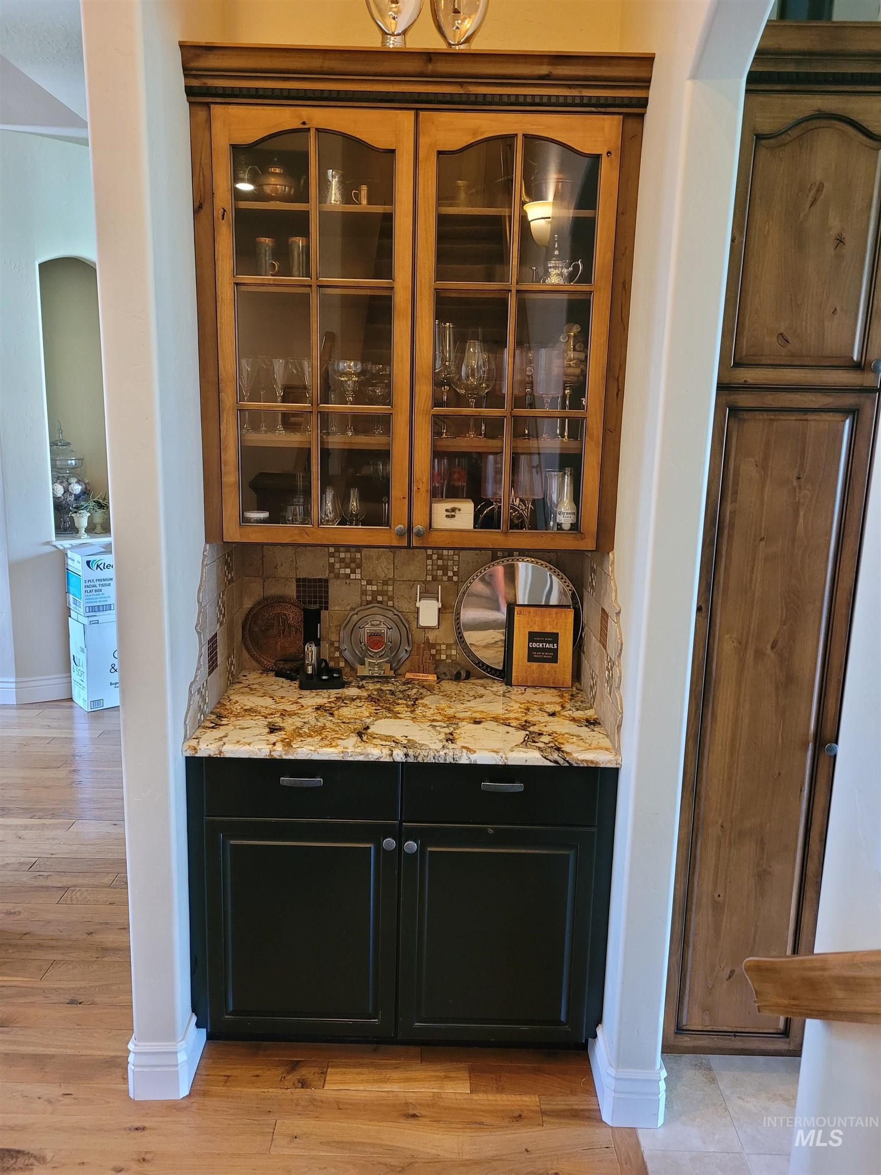 Bar area featuring dark cabinets, light stone countertops, and glass insert cabinets