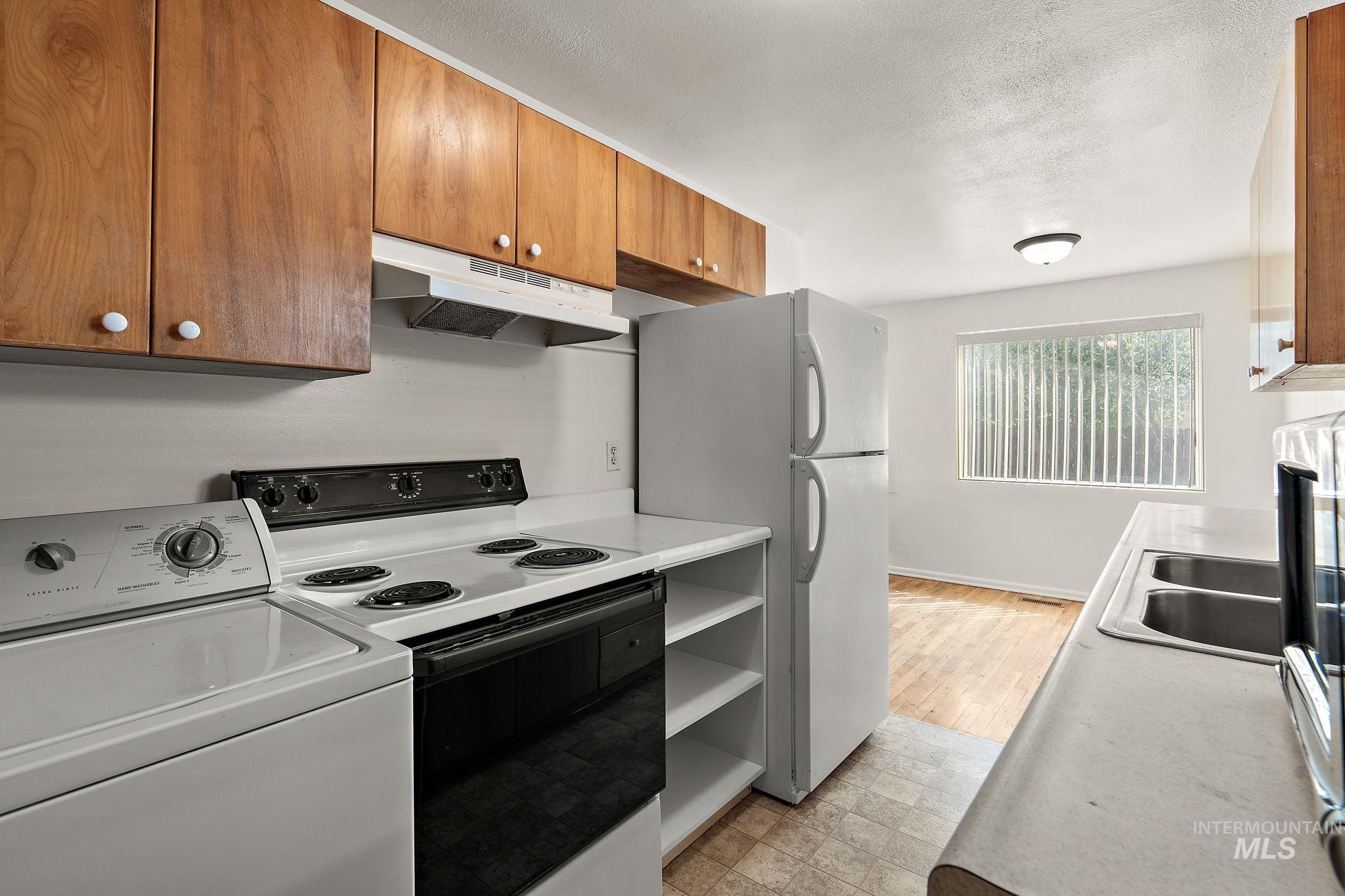 Kitchen featuring washer / dryer, white appliances, under cabinet range hood, light countertops, and a textured ceiling
