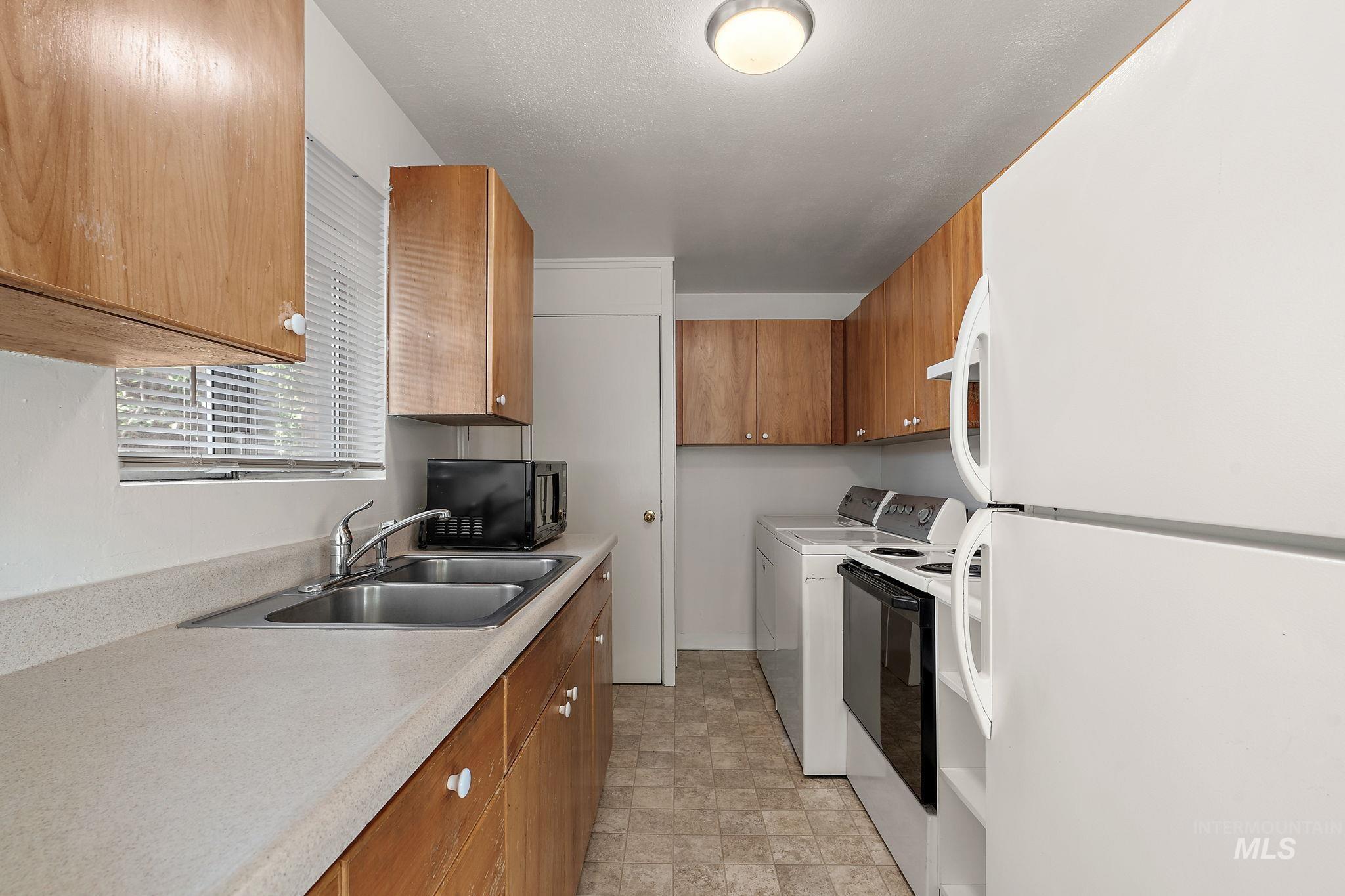 Kitchen with white appliances, brown cabinets, light countertops, and washer / dryer