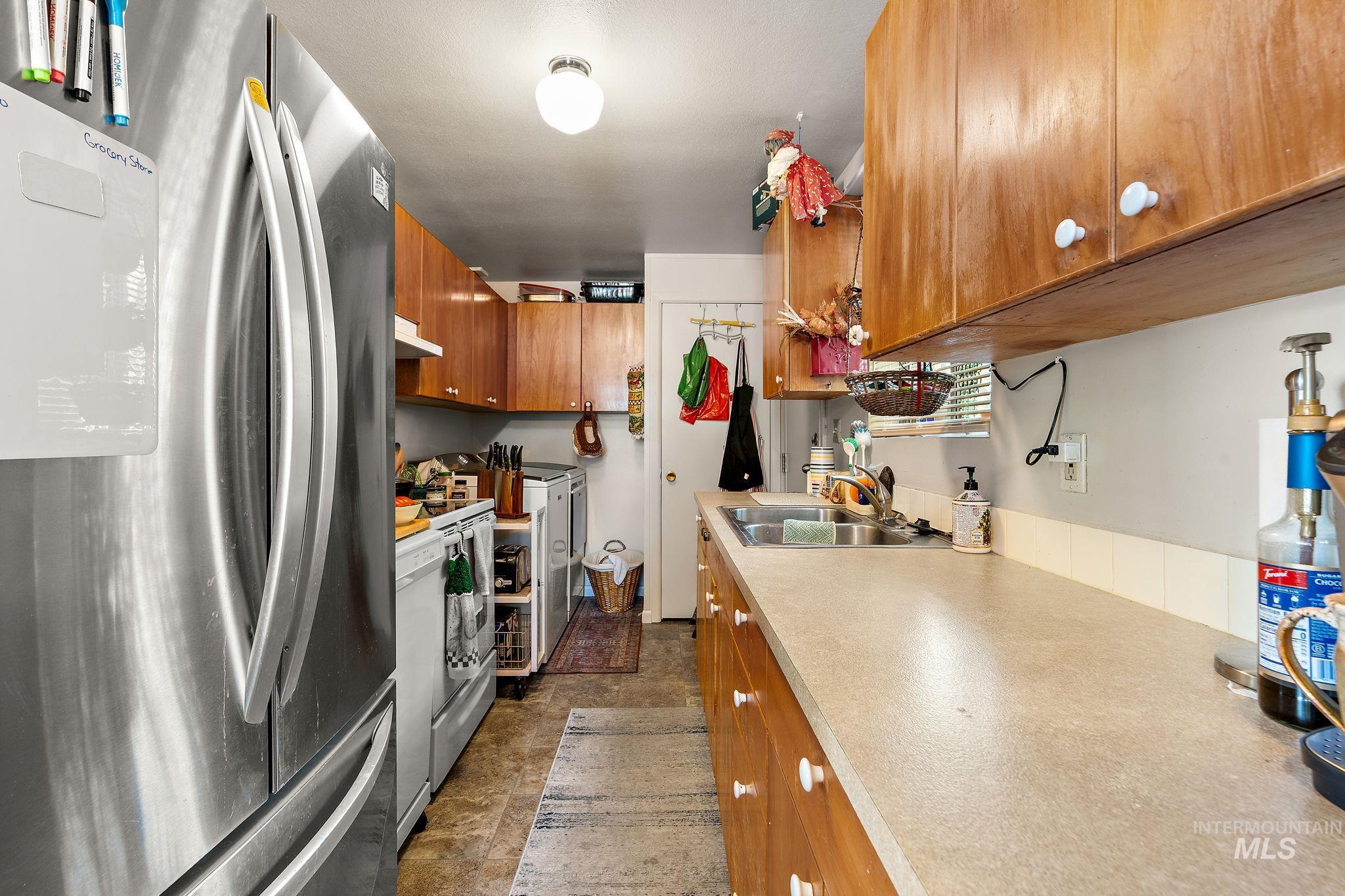 Kitchen with freestanding refrigerator, brown cabinets, light countertops, electric stove, and under cabinet range hood