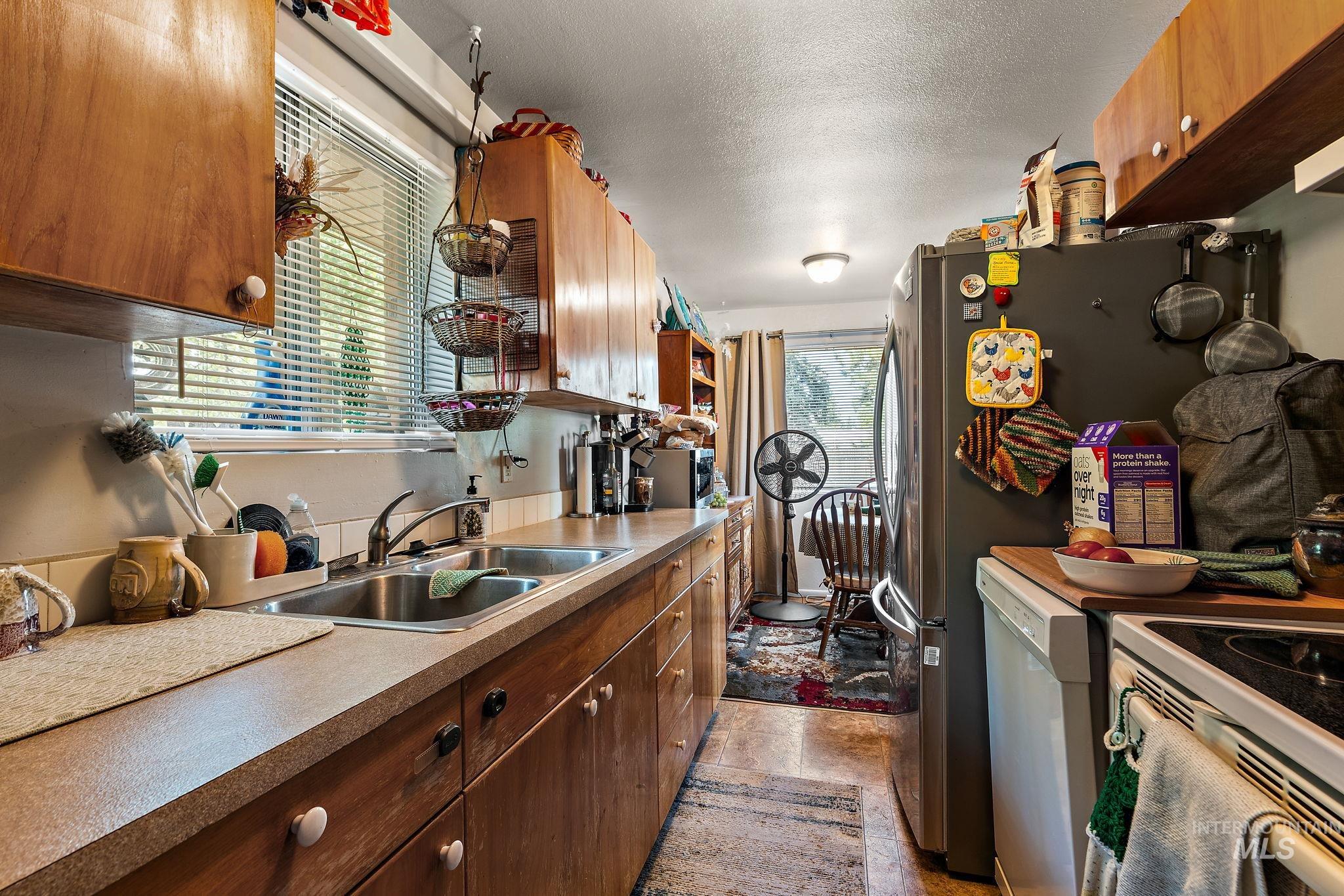 Kitchen featuring a textured ceiling, white appliances, light countertops, and brown cabinets