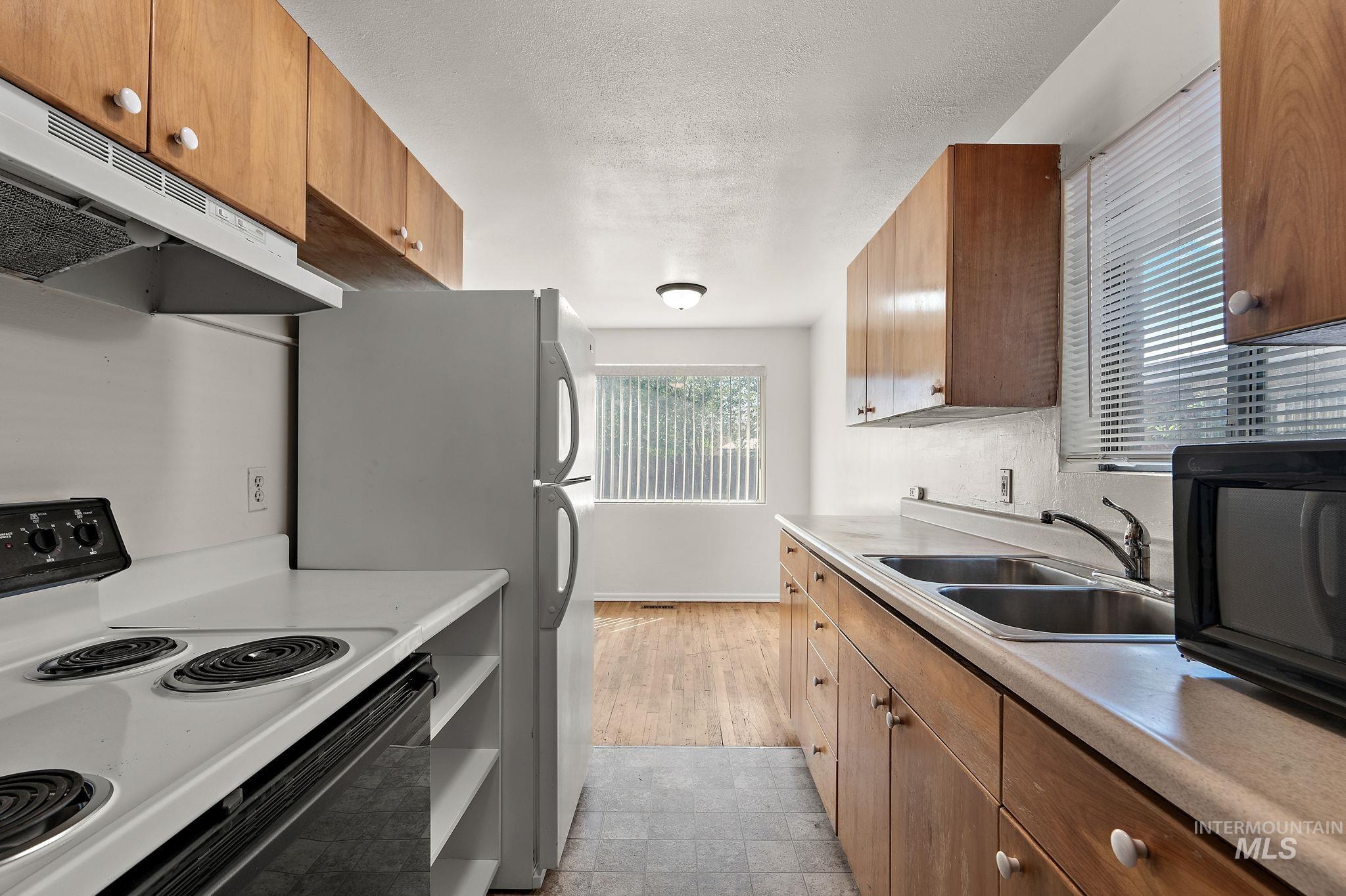 Kitchen with electric range, brown cabinets, light countertops, under cabinet range hood, and a textured ceiling