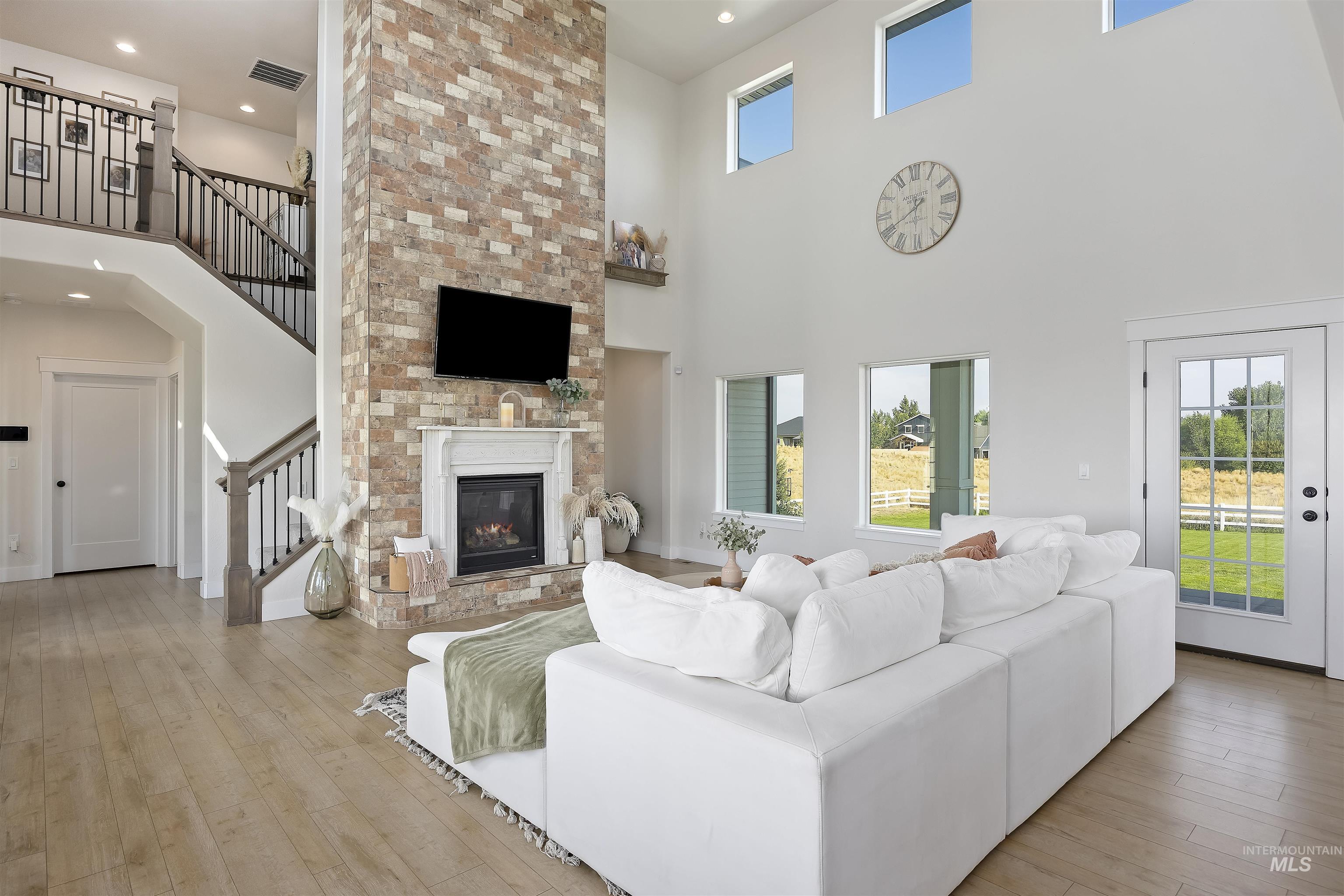 Living area featuring light wood-style flooring, a high ceiling, stairway, recessed lighting, and a large fireplace