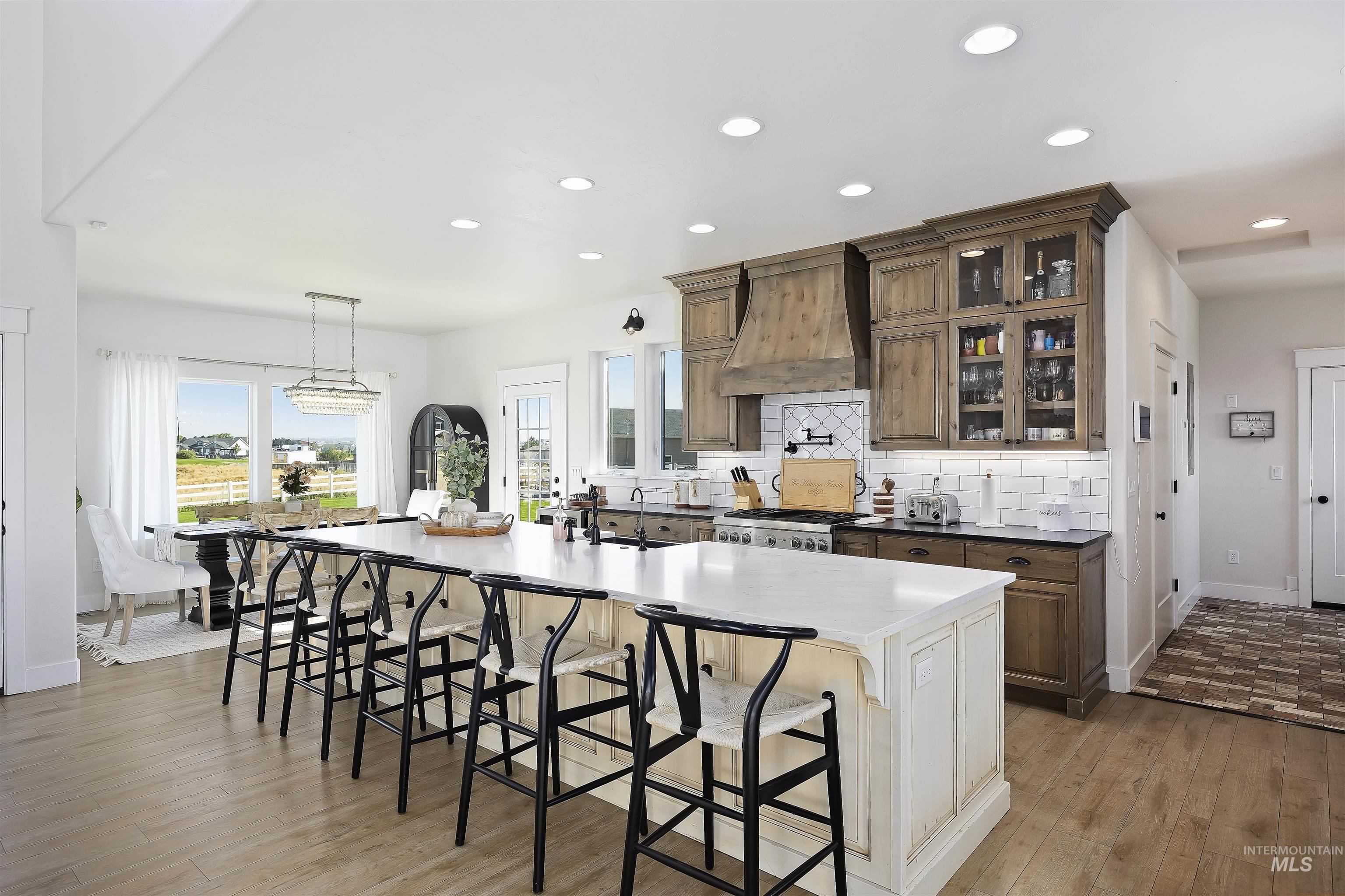 Kitchen featuring a large island with sink, a kitchen bar, tasteful backsplash, glass insert cabinets, and recessed lighting