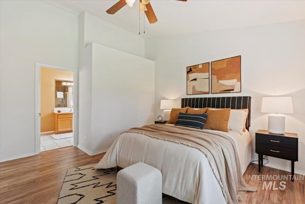 Bedroom featuring light wood-type flooring, a ceiling fan, connected bathroom, and high vaulted ceiling