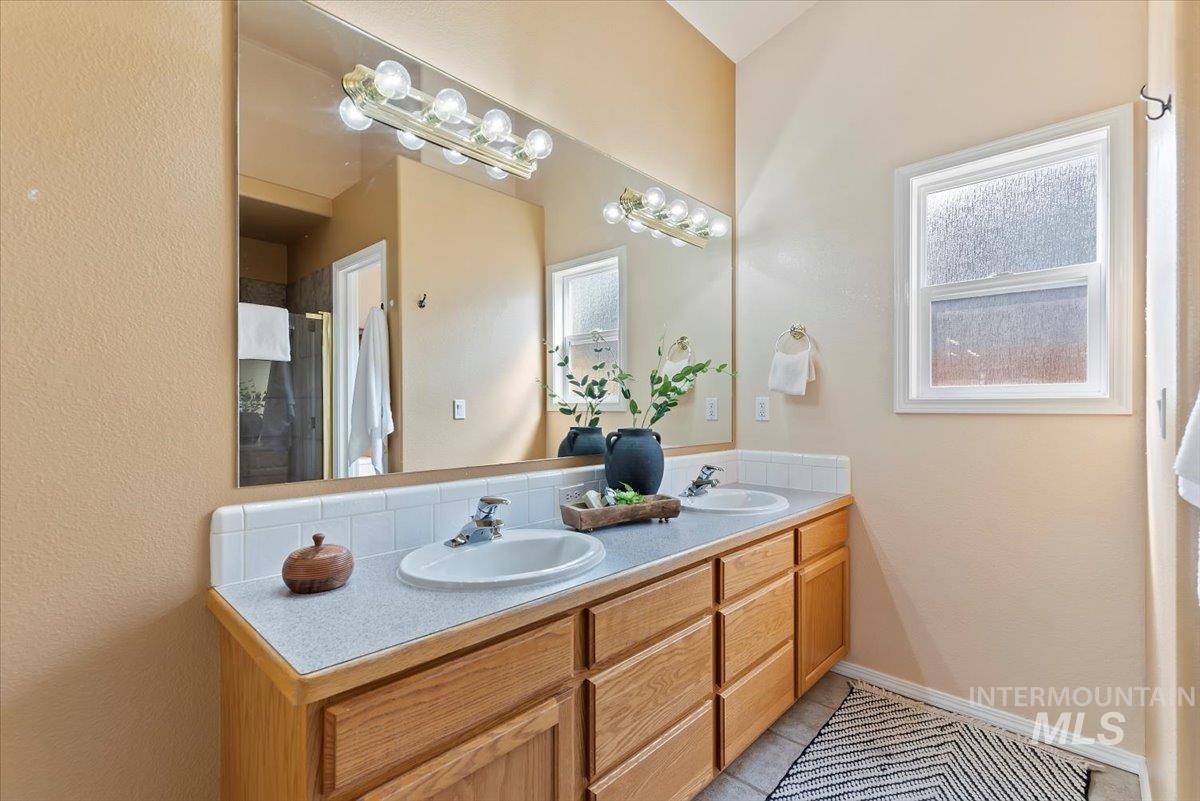 Full bath with double vanity, light tile patterned floors, and a shower