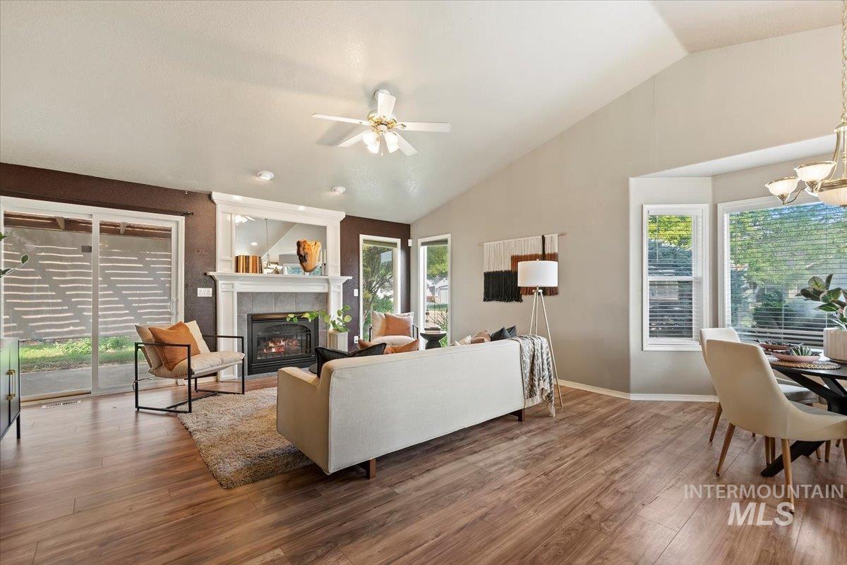 Living room with lofted ceiling, wood finished floors, a tiled fireplace, a chandelier, and ceiling fan