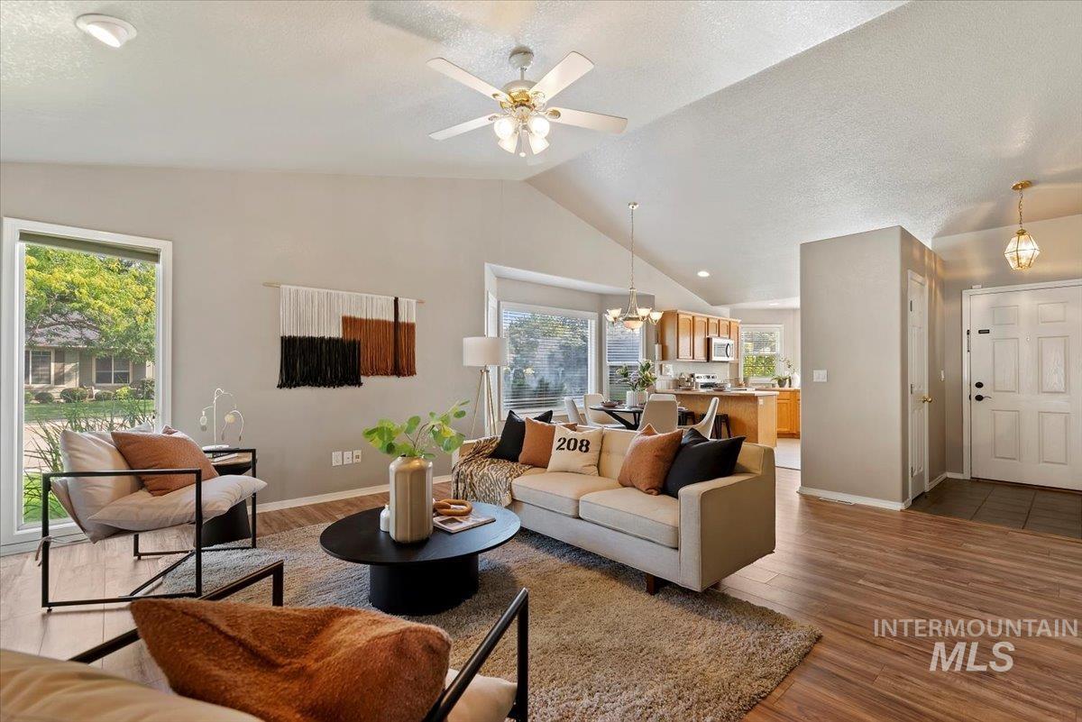 Living room featuring a textured ceiling, wood finished floors, a chandelier, ceiling fan, and high vaulted ceiling