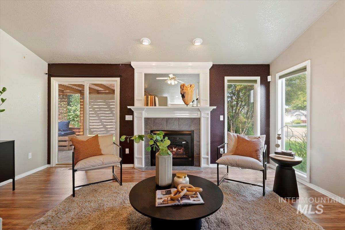 Living area with a tiled fireplace, wood finished floors, and ceiling fan