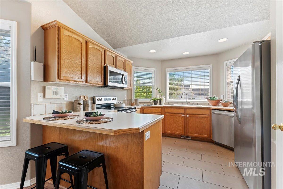 Kitchen featuring a peninsula, light countertops, a breakfast bar, appliances with stainless steel finishes, and a textured ceiling